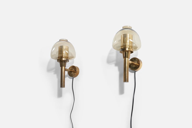 A pair of brass and glass wall lights / sconces, designed by Hans-Agne Jakobsson for his own firm in Markaryd, Sweden. c. 1960s-1970s.

Dimensions listed are with shades. Back plate diameter is 4 inches.