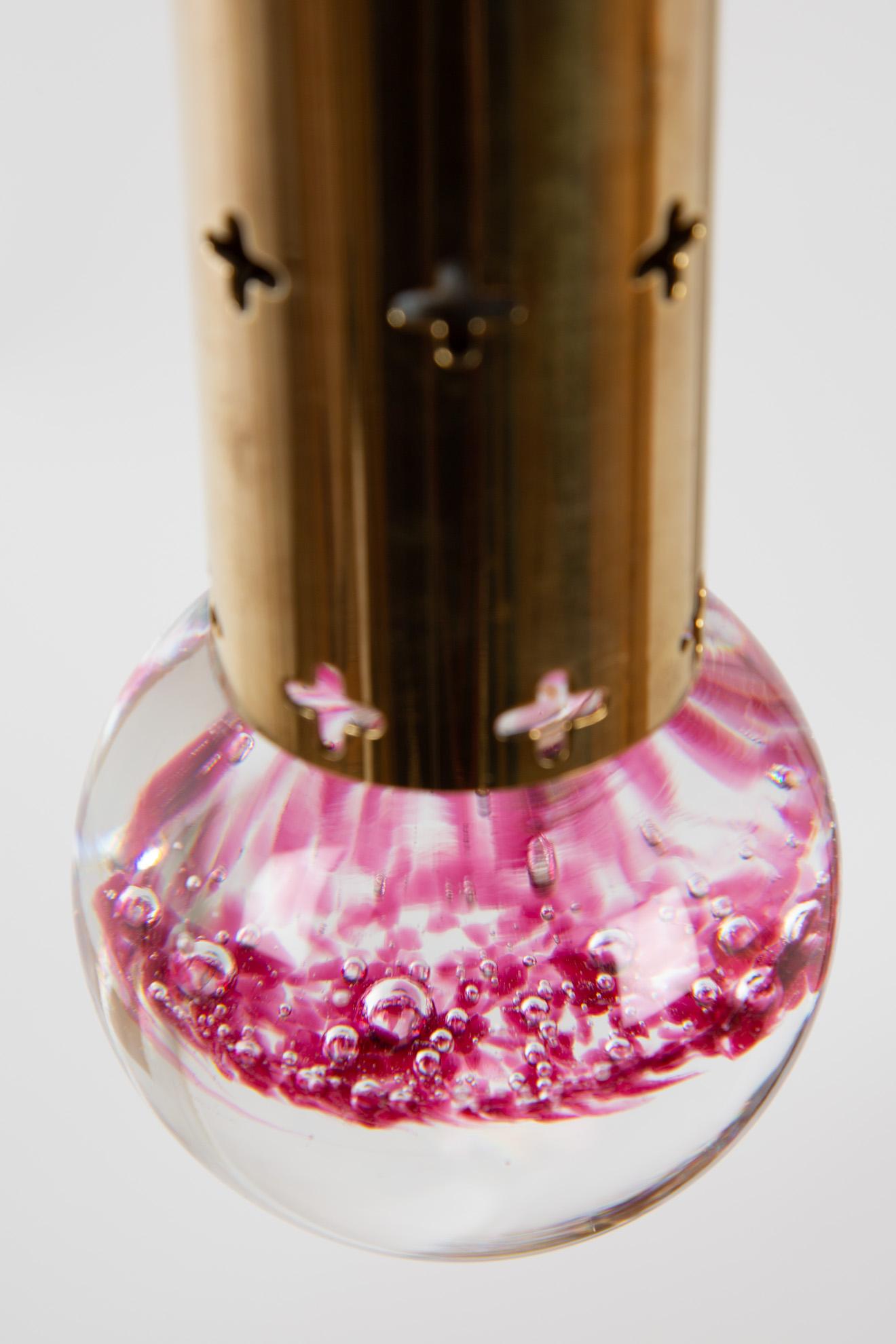 Hans Agne Jakobsson pendant brass with glass drop. In the glass drop is pink colored glass enclosed. It is like a landscape. The brass tube has some stars. The light is twinkling through the stars.
