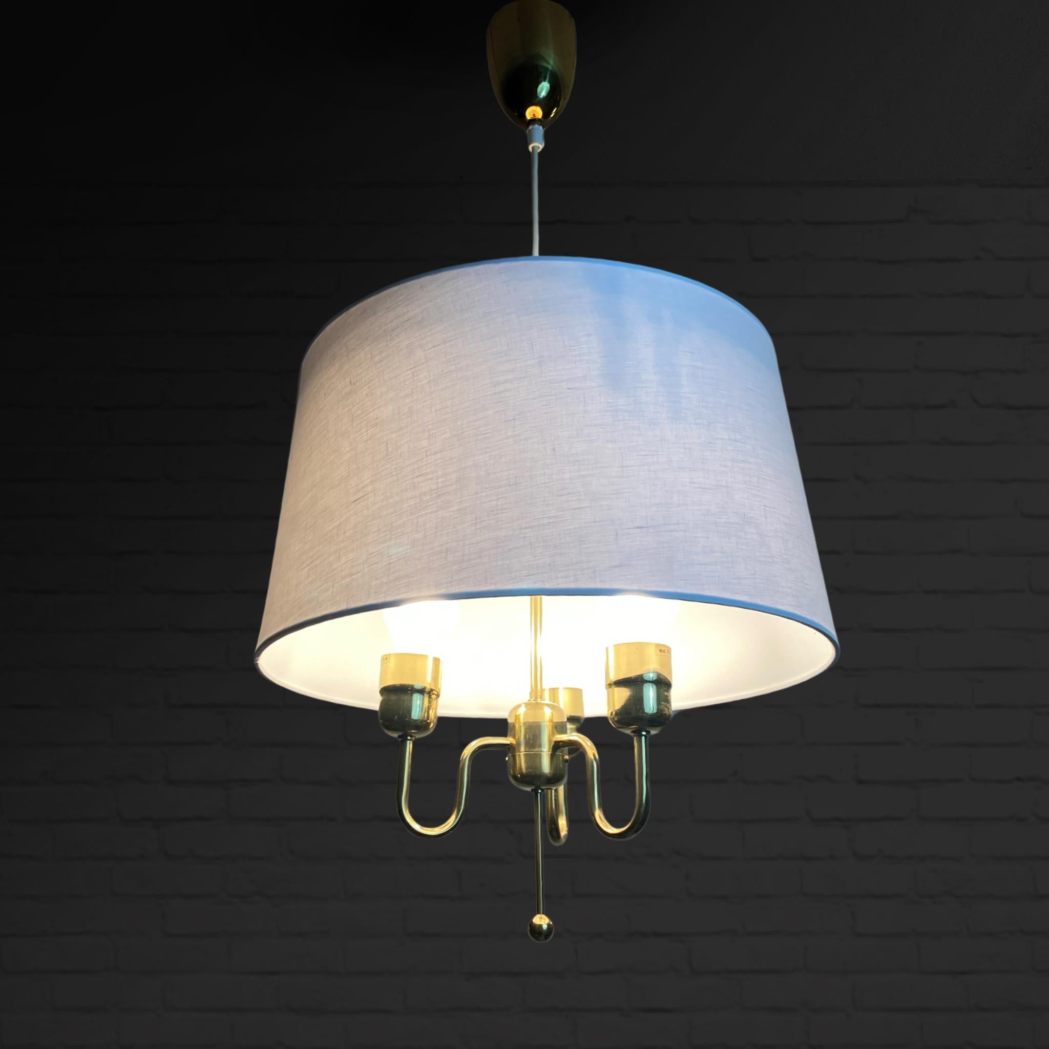 Elegant pendant lamp model T883 by Hans-Agne Jakobsson. Crafted from brass, it features three lamp holders and a textile-covered shade, complete with the original bullet-shaped canopy. The lamp shade has been replaced. Swedish industrial designer