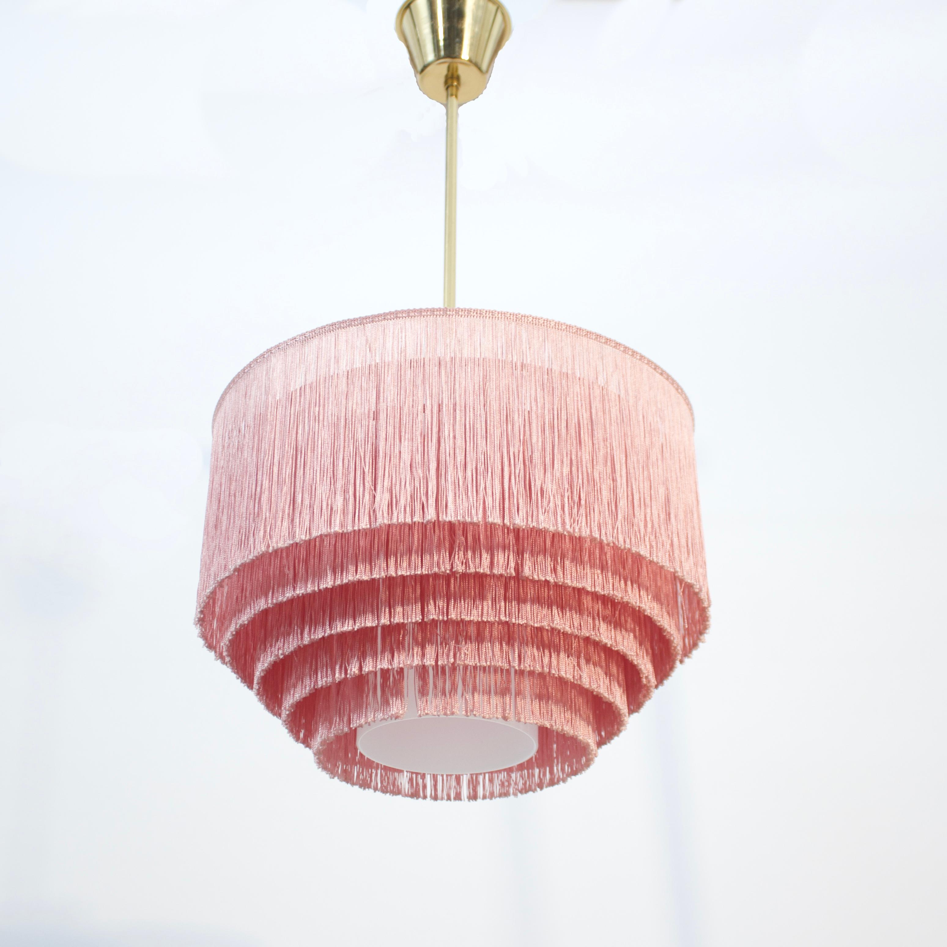 Rara variación de lámpara de techo de la famosa lámpara de flecos diseñada por Hans-Agne Jakobsson para su propia empresa en la década de 1960. Tulipa interna de cristal opalino que sujeta la bombilla. Flecos rosas. Todo ello montado sobre un