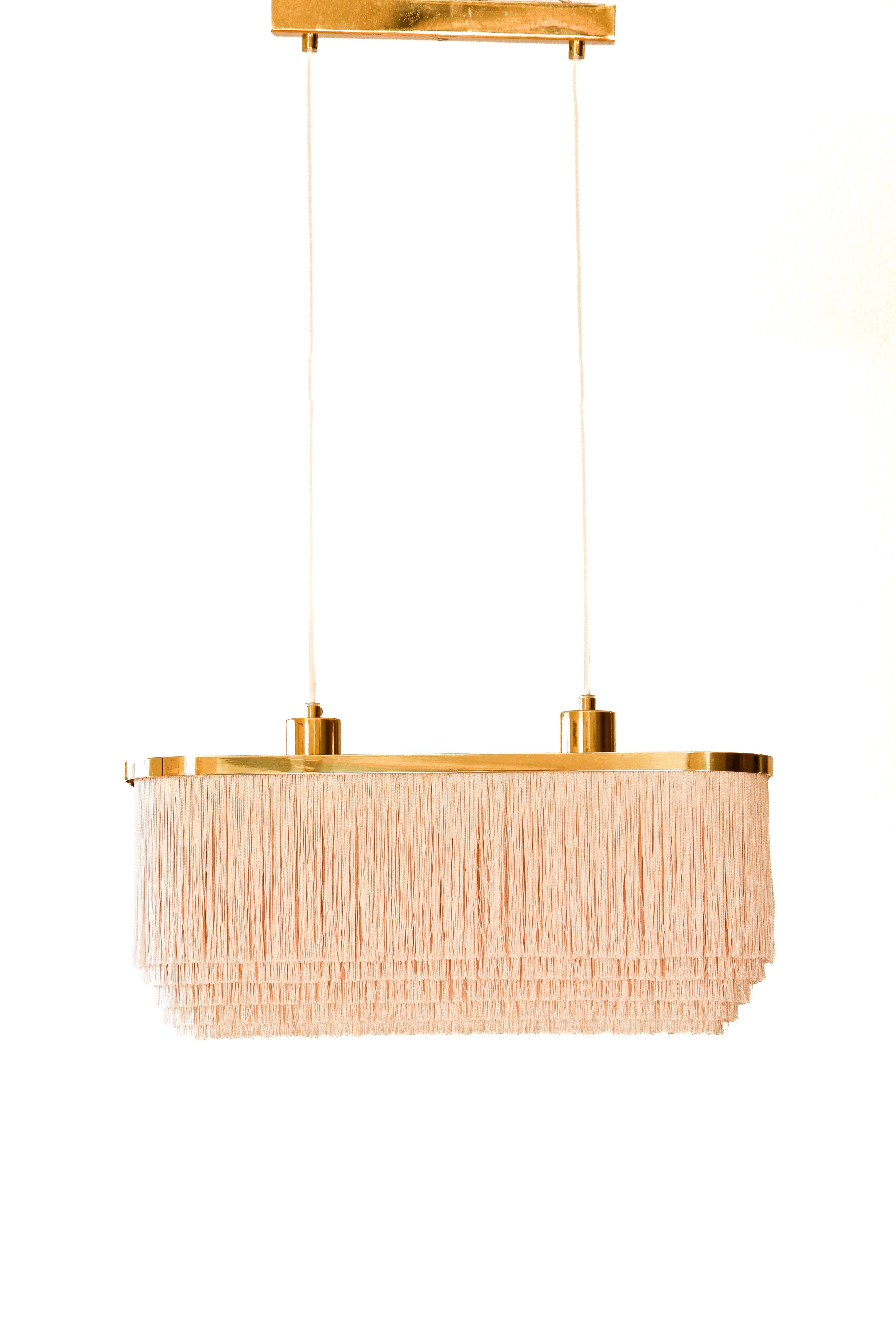 Rara lampada a frangia di Hans-Agne Jakobsson realizzata in seta con anima in ottone. Nella parte superiore della lampada viene utilizzato un plexiglass per riflettere la luce. Questo modello è una delle icone della collezione di frange di Hans-Agne