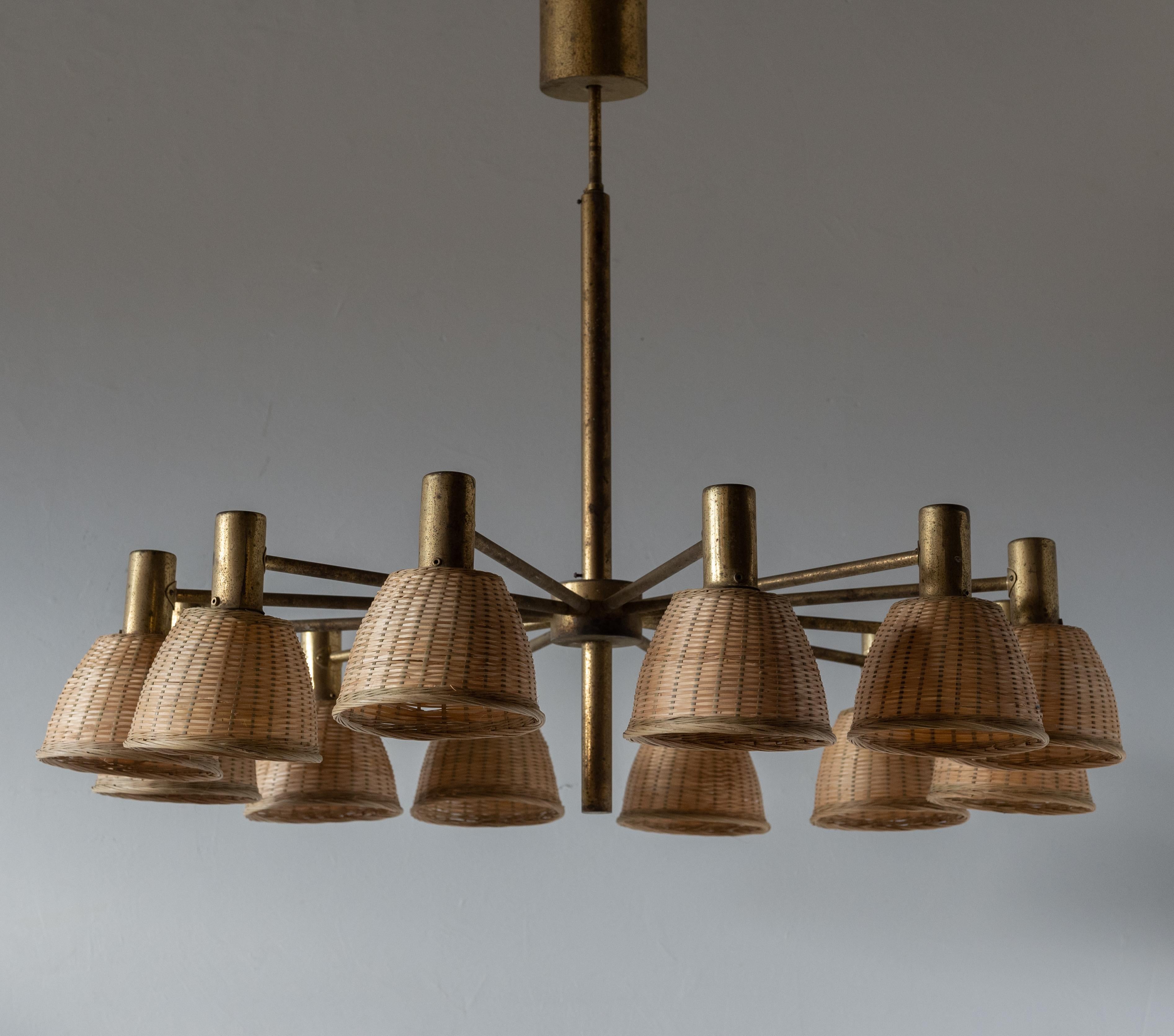 A sizable 12-armed chandelier, designed by Hans-Agne Jakobsson for his own firm in Markaryd, Sweden. c. 1960s. Features brass and assorted vintage rattan lampshades. Likely originally mounted with glass lampshades.

Presents with beautiful and