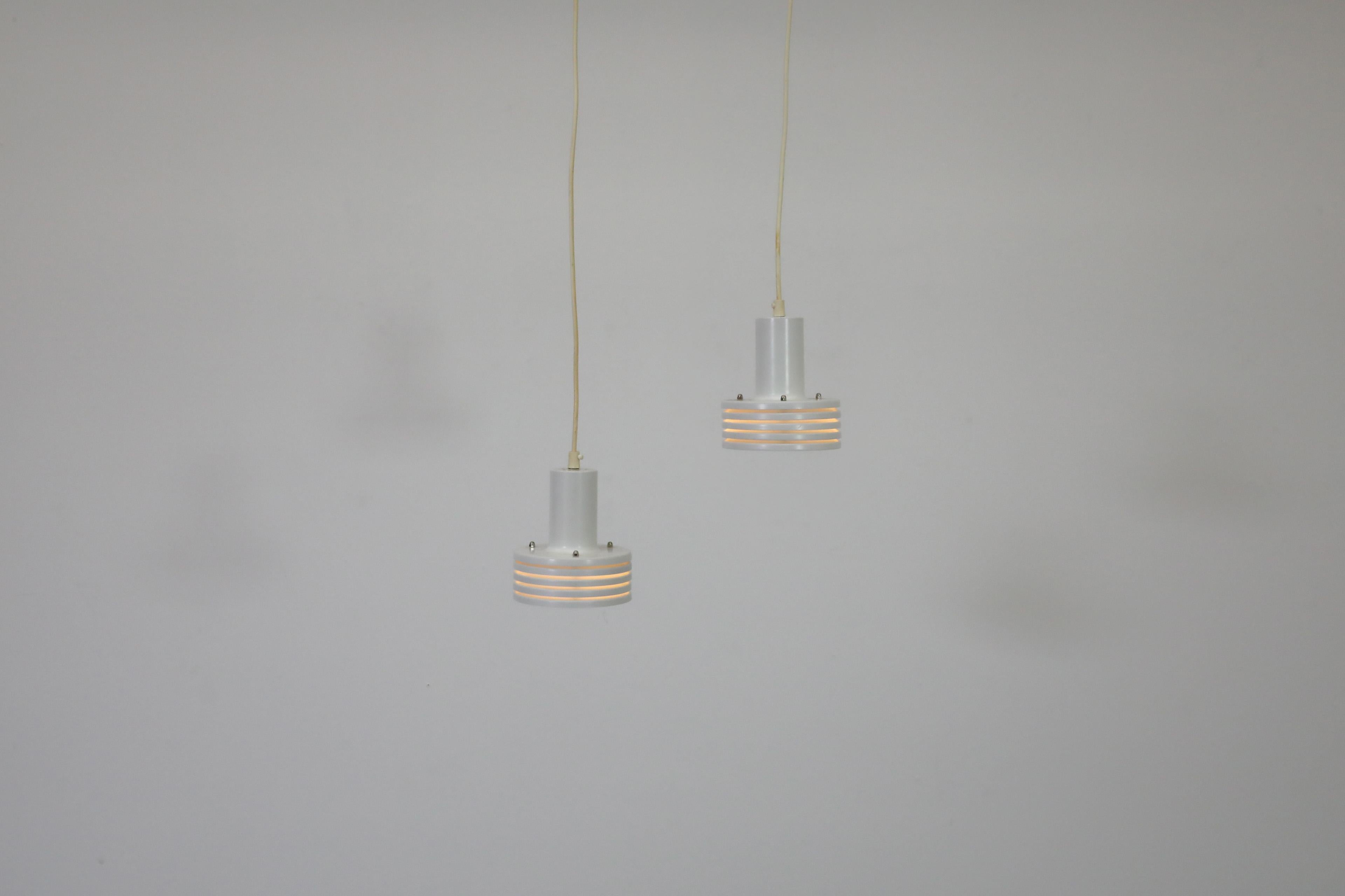 Mid-Century Hans-Agne Jakobsson inspired white enameled metal pendant lights with multi-tiered barrel shade. Attractive pendants with off-white cords perfect for providing ambient lightning to a cozy space or entry way.  In original condition with