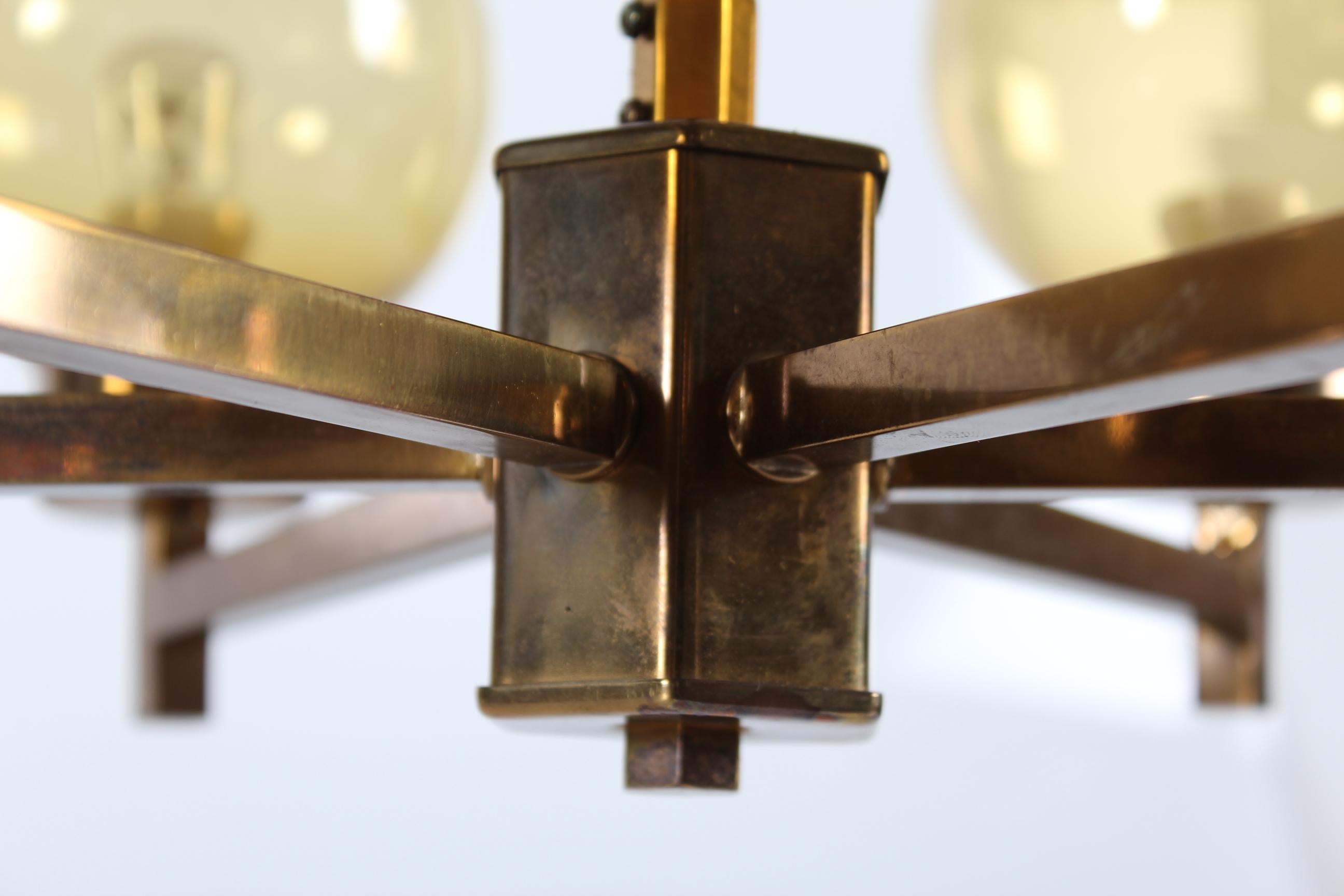 Lampadario a sei bracci in stile Hans-Agne Jakobsson.
Il lampadario ha una struttura in ottone patinato montata con 6 globi di vetro soffiato a bocca di colore ambrato.

Sulla cornice sono impresse le iniziali G.K.

La lampada da soffitto è in