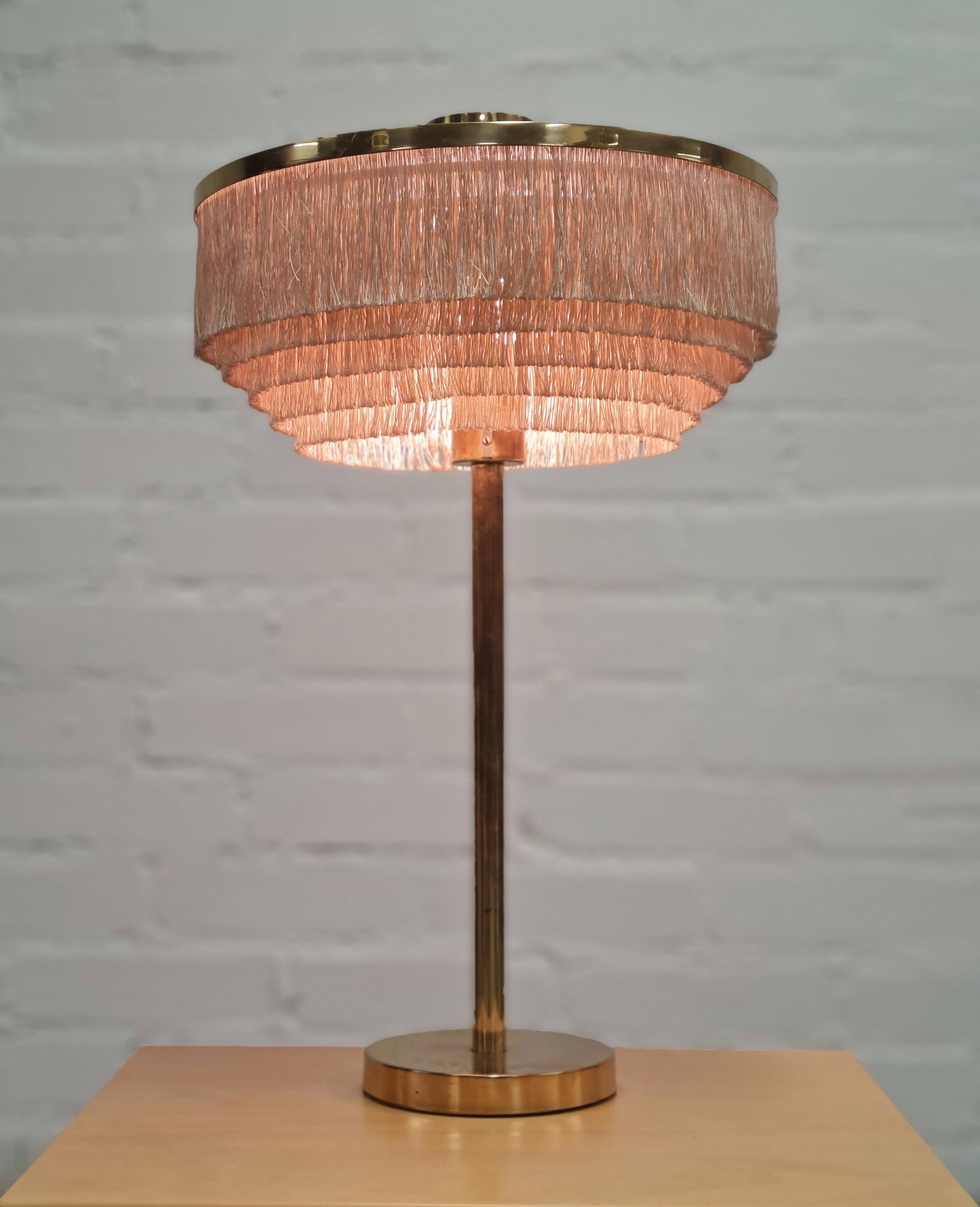A beautiful example of the Hans-Agne Jakobsson table lamp model B-138 in brass and string fringes. The lamp stands at over 60cm and is quite presentable. The fringes add a soft playful touch to the rigid brass body, which makes it easier to