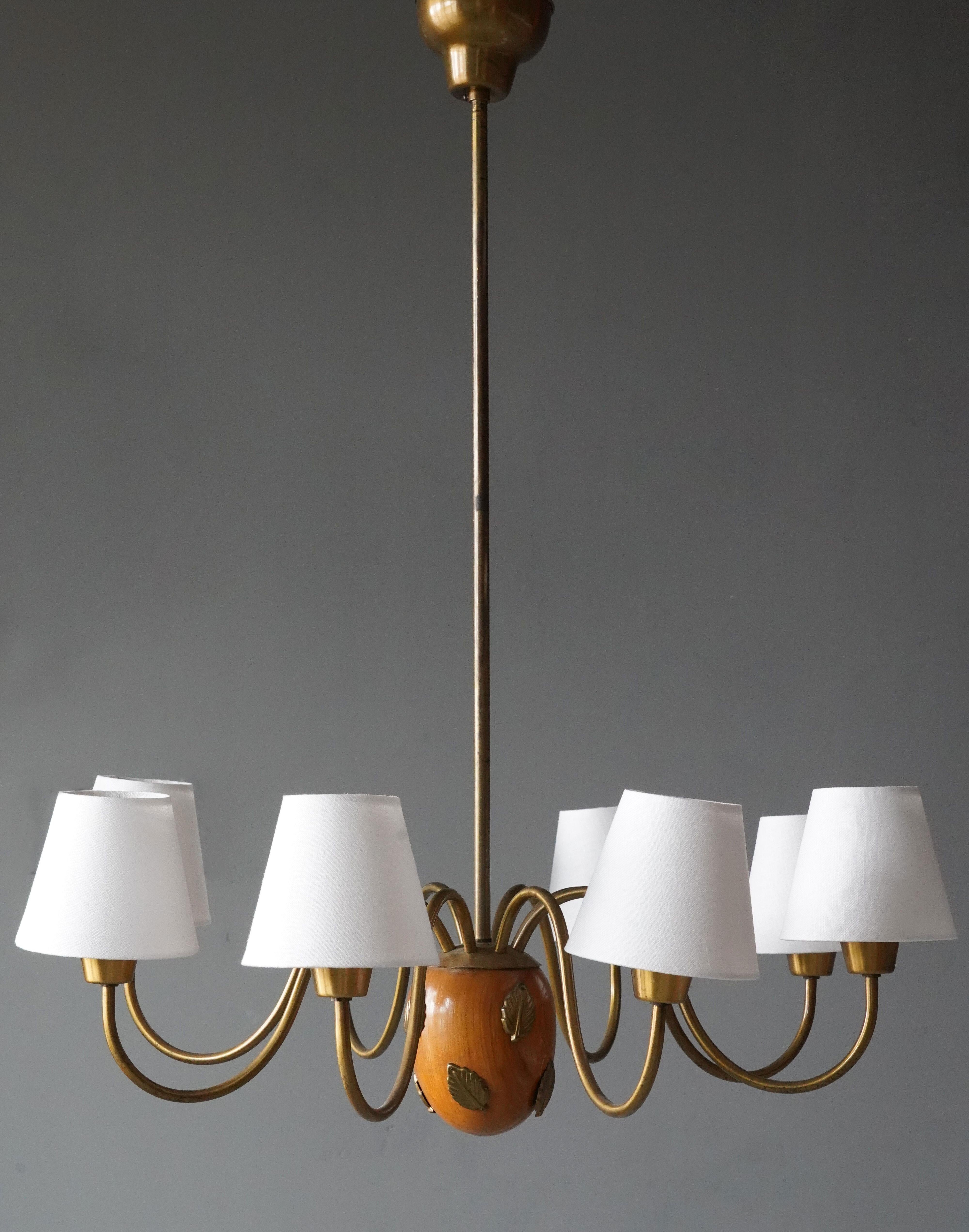 A sizable 8-armed chandelier. Designed by Swedish Hans Bergström. Produced by his own firm Ateljé Lyktan, Sweden, 1940s. Features brass, turned wood with brass ornaments, and white fabric lampshades.

Stated dimensions include lampshades. Brand