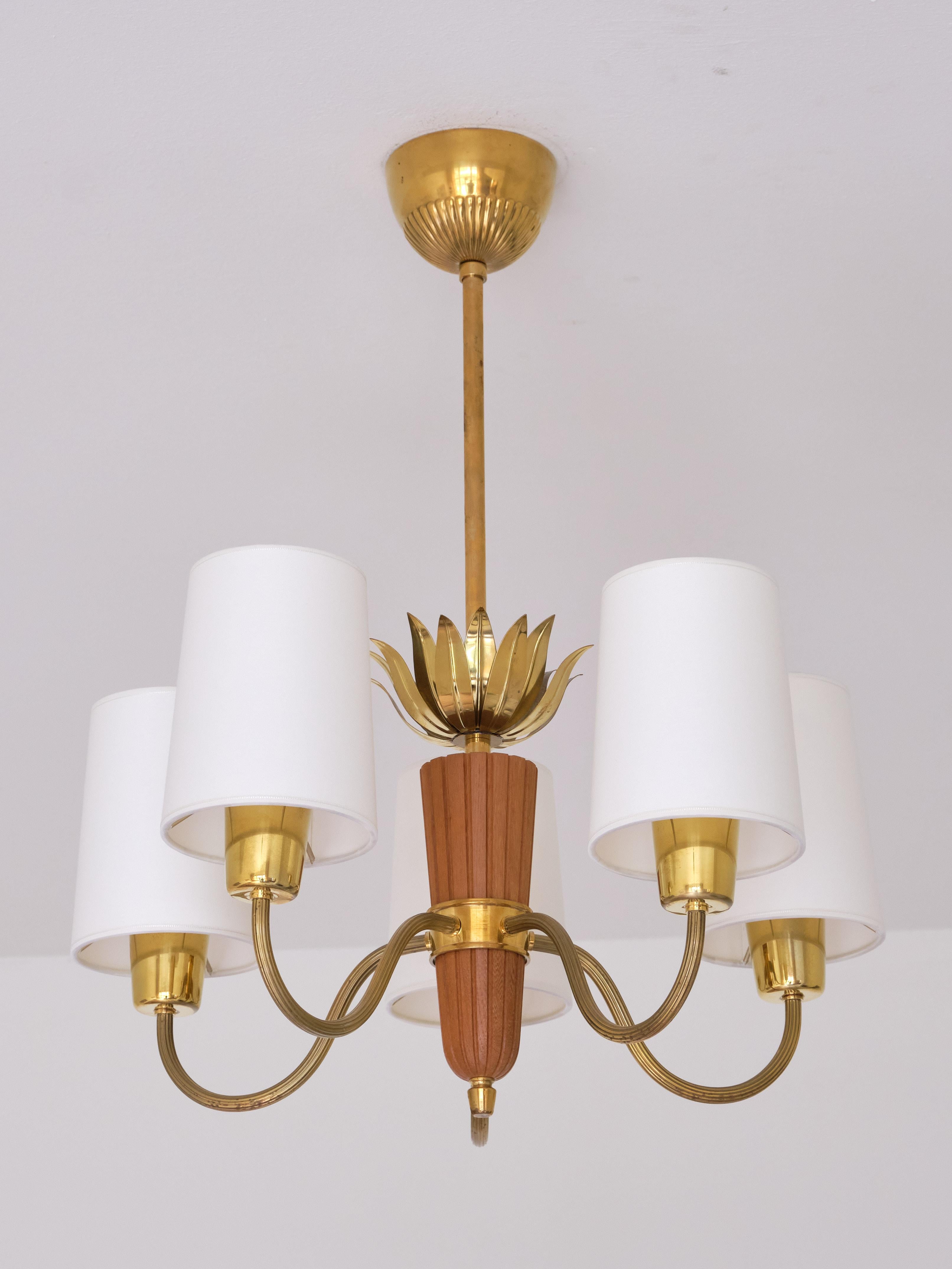 This elegant five arm chandelier was produced by ASEA in Sweden in the 1950s. The lamp consists of a brass stem, a carved oak centerpiece to which the five arms are attached. The decorative brass leaves attached to the stem and the five sculpted and