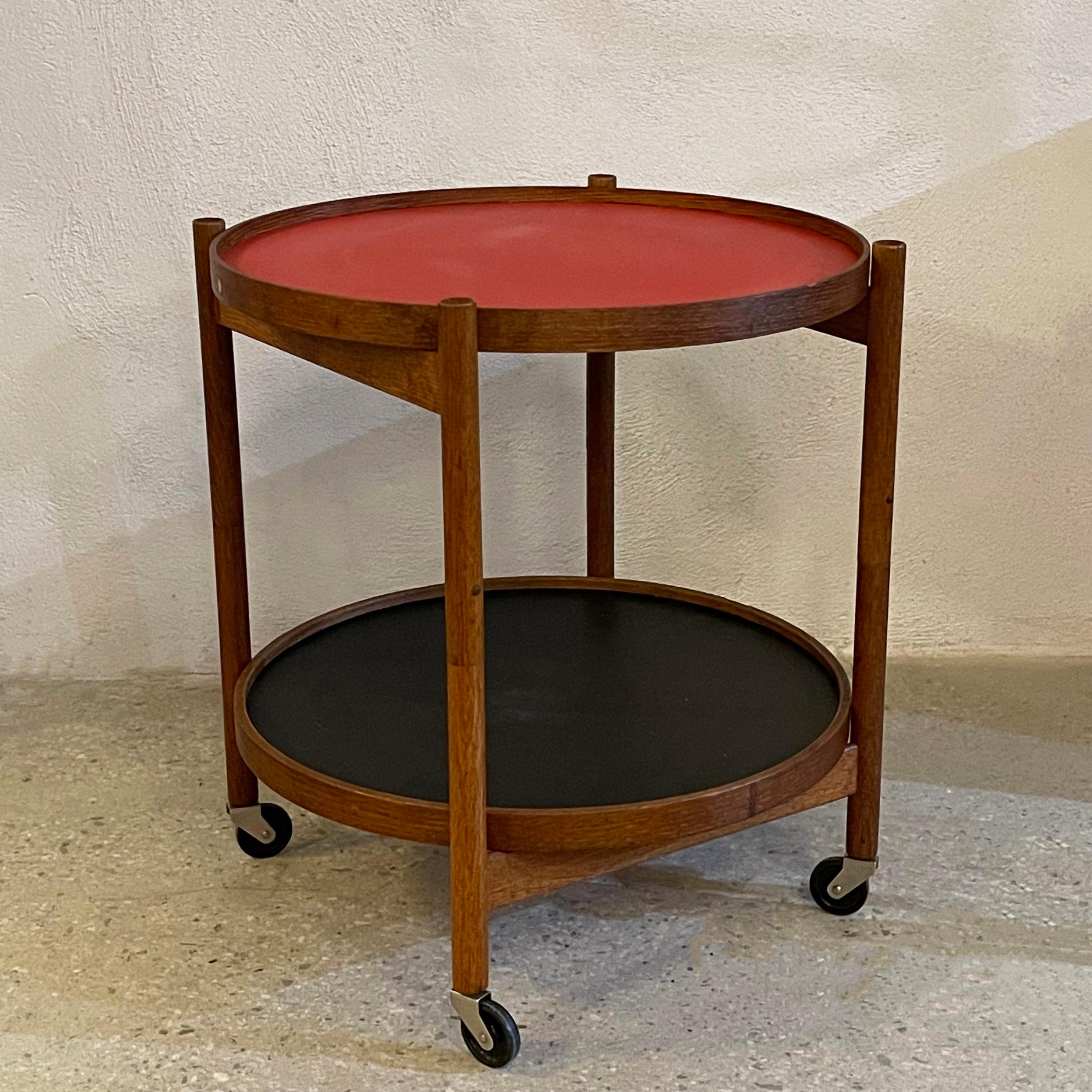 Scandinavian modern, rolling, bar or serving cart trolley by Danish architect Hans Bølling for Torben Ørskov features two oak trimmed, round reversible trays that are lacquered red on one side and black on the other that fit into a collasping oak