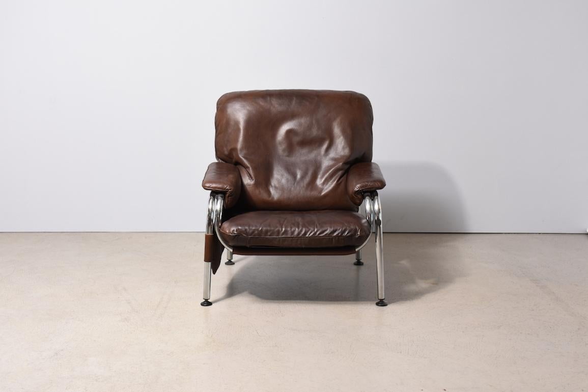 Kangaroo Armchair by Swiss designer Hans Eichenberger.  Frame made of chromed metal tube. Armchair cover in brown leather. On right armchair side pocket for magazine or book shelf. Designed in 1970 for the 