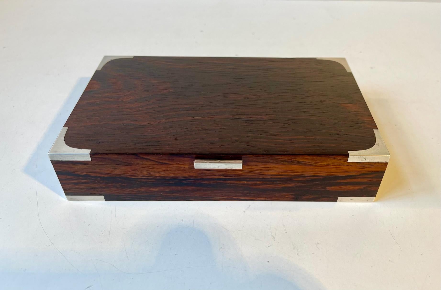 One-compartment Rosewood box for playing cards, jewelry, cigars, cigarettes etc. Its manufactured by the Danish Silversmith Hans Hansen circa 1950-60. The corners, hinge and lid-mechanism is made from 925 sterling silver. It has an easy removable