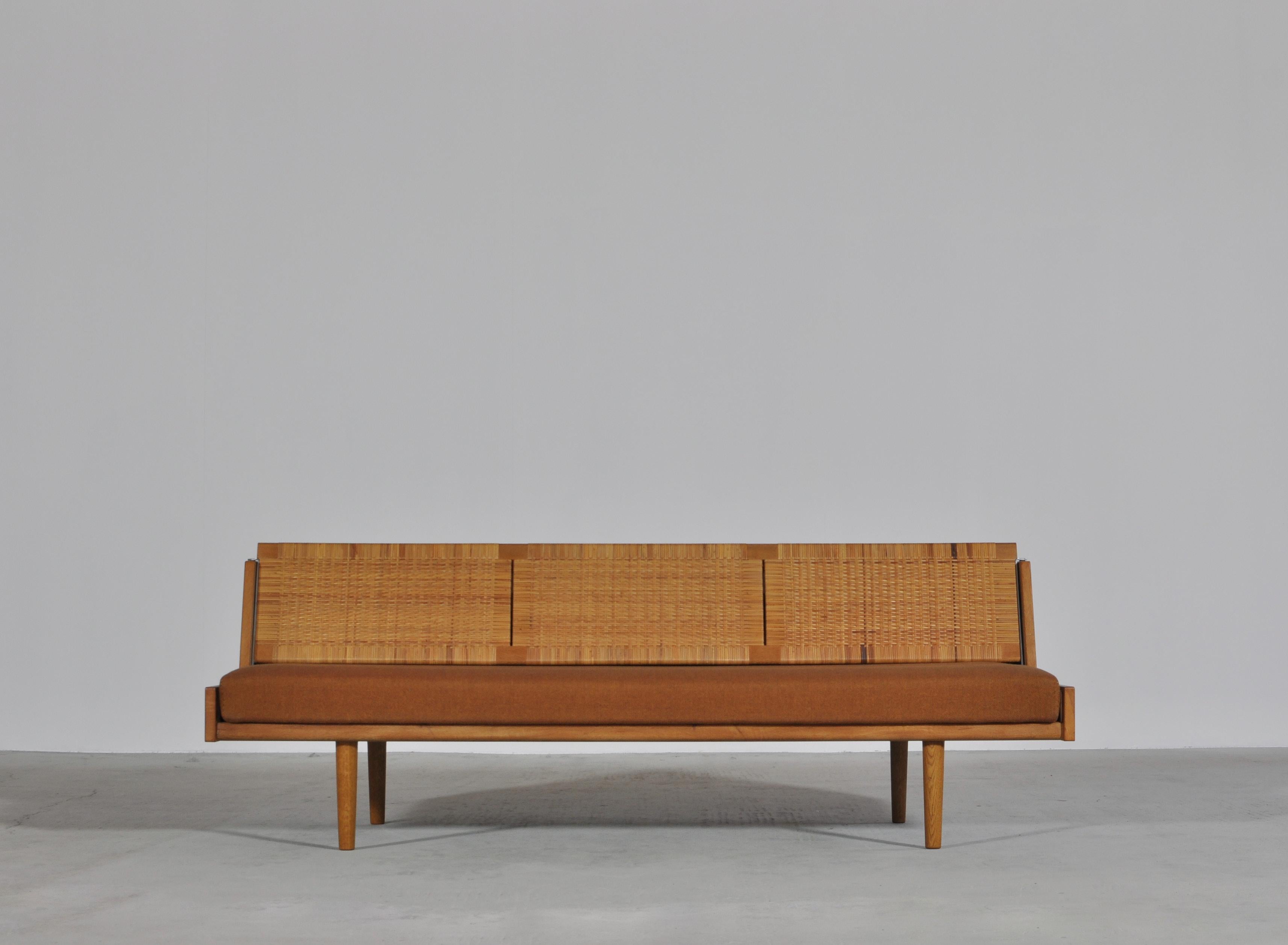 Designed by Hans Wegner for GETAMA this amazing convertible daybed / sofa features a beautifully patinated oak frame and woven cane / rattan back seat which reveals a hidden space for blankets, pillows etc. The model GE-7 was designed by Wegner in