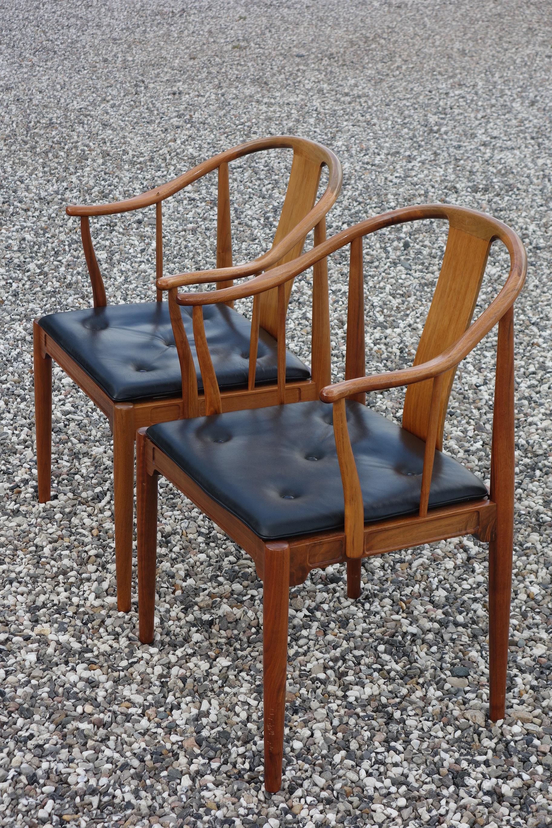 Hans J. Wegner: A pair of flamed walnut armchairs “China chairs”. Loose seat cushion upholstered with black leather, fitted with buttons. Model 4283. Designed 1944. Manufactured 1977 by Fritz Hansen with maker's silver plaque in back. The China