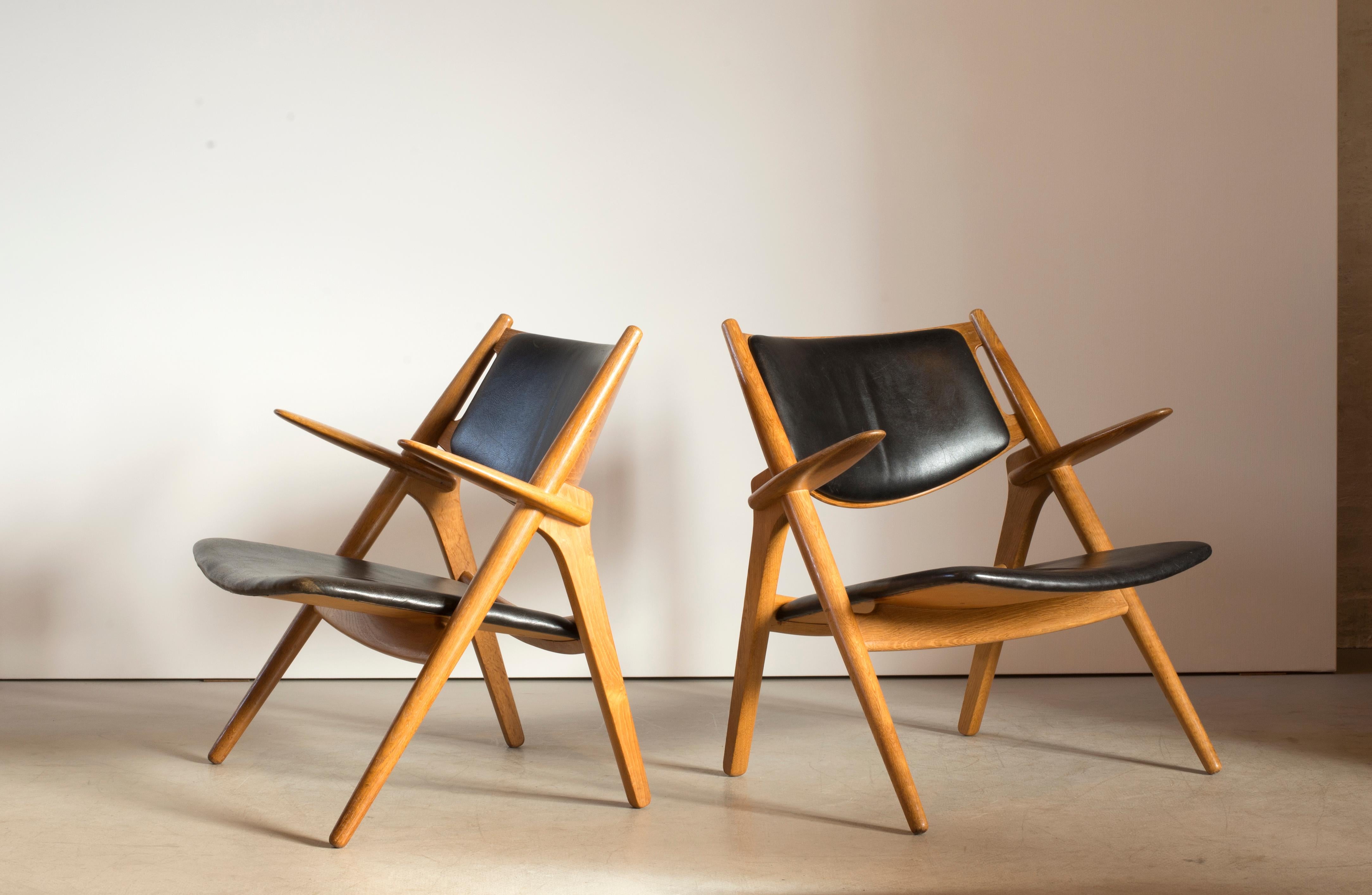 A pair of armchairs with frame of patinated oak. Seat and back upholstered with black leather. Model CH28. Executed by Carl Hansen & Søn, stamped by maker.