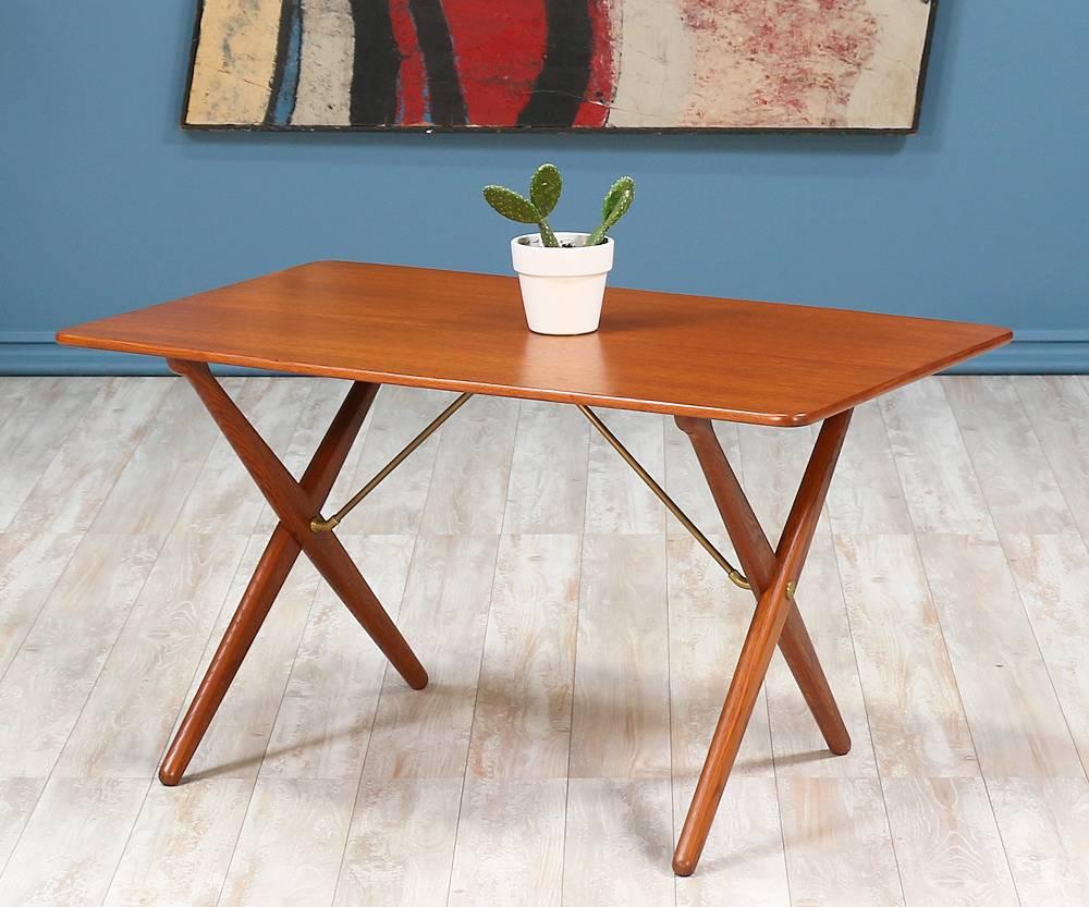 Iconic coffee table designed by Hans J. Wegner for Andreas Tuck in Denmark circa 1950’s. Comprised of a teak wood, this table features saber x-shaped legs with patinated brass braces that support the top. This beautiful Danish Modern design is ideal