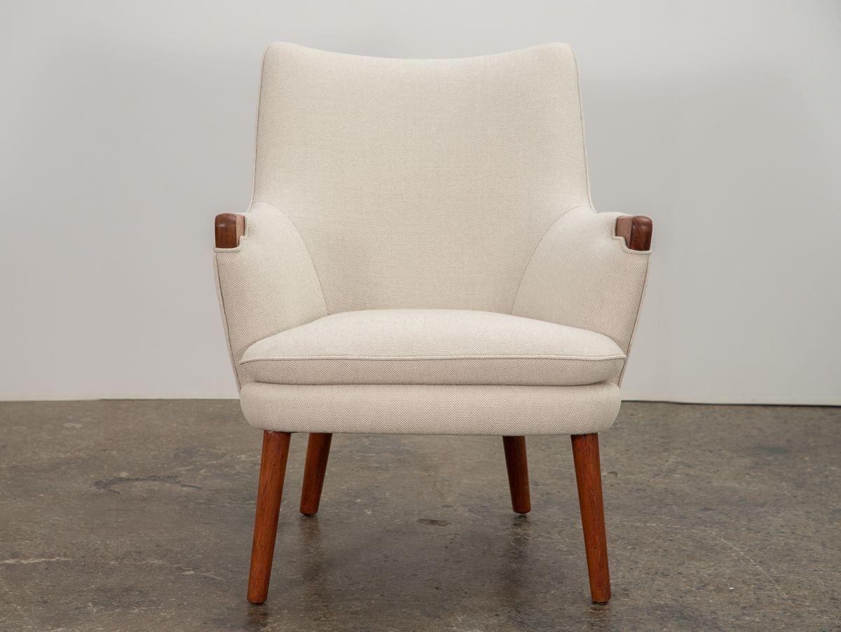 Una escasa silla modelo AP-20, diseñada por Hans J. Wegner, fabricada por AP Stolen. La forma clásica se acentúa con esculturales asas de teca en los reposabrazos. Nuestro ejemplar ha sido fielmente restaurado y tapizado en Hallingdal 65 de época en
