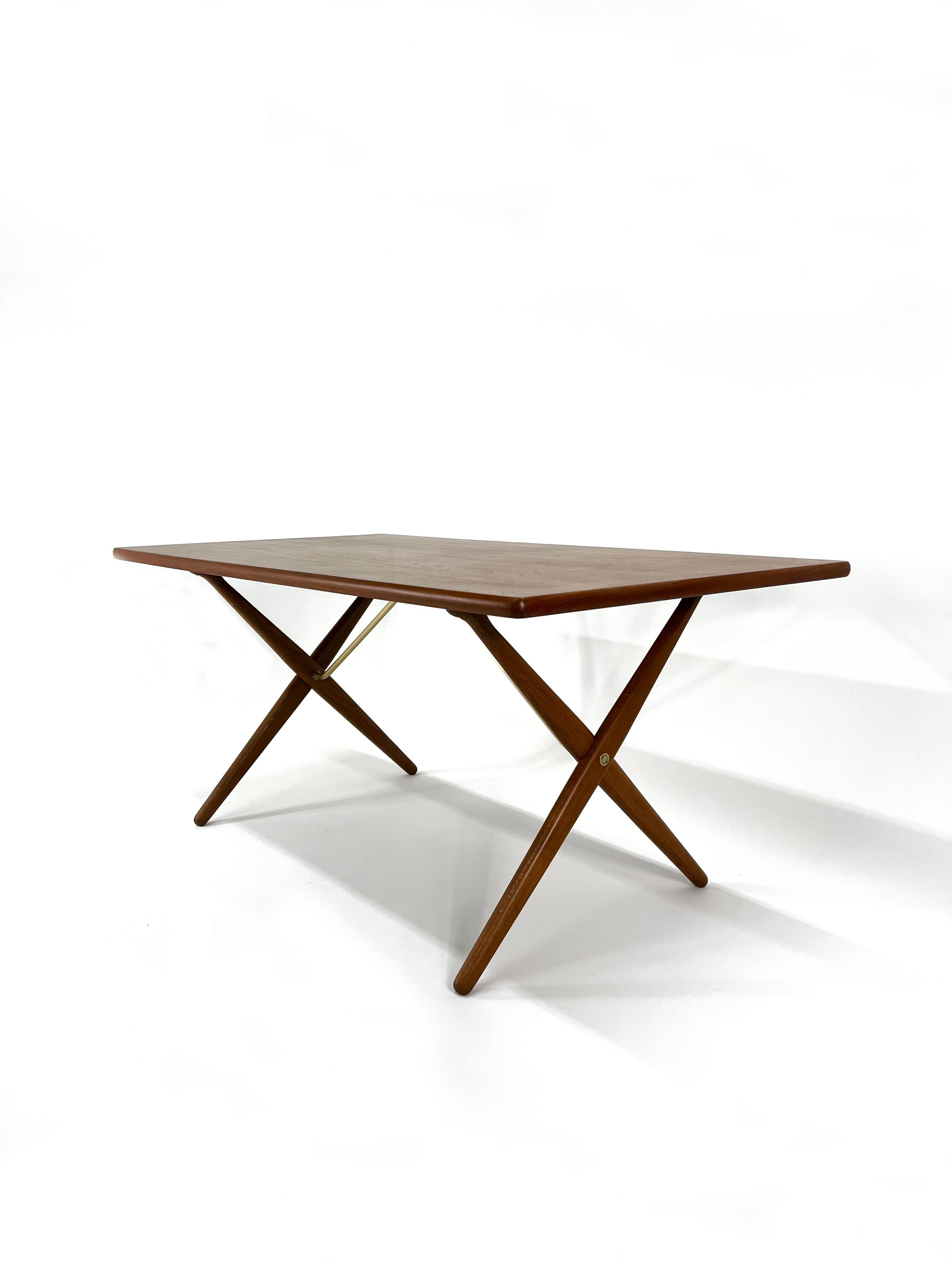 Cette magnifique table de salle à manger à pieds croisés, conçue par Hans J. Wegner pour Andreas Tuck, en teck, chêne et laiton, est également connue sous le nom de table Sabre.  Wegner a conçu cette pièce magnifique et fonctionnelle qui est très