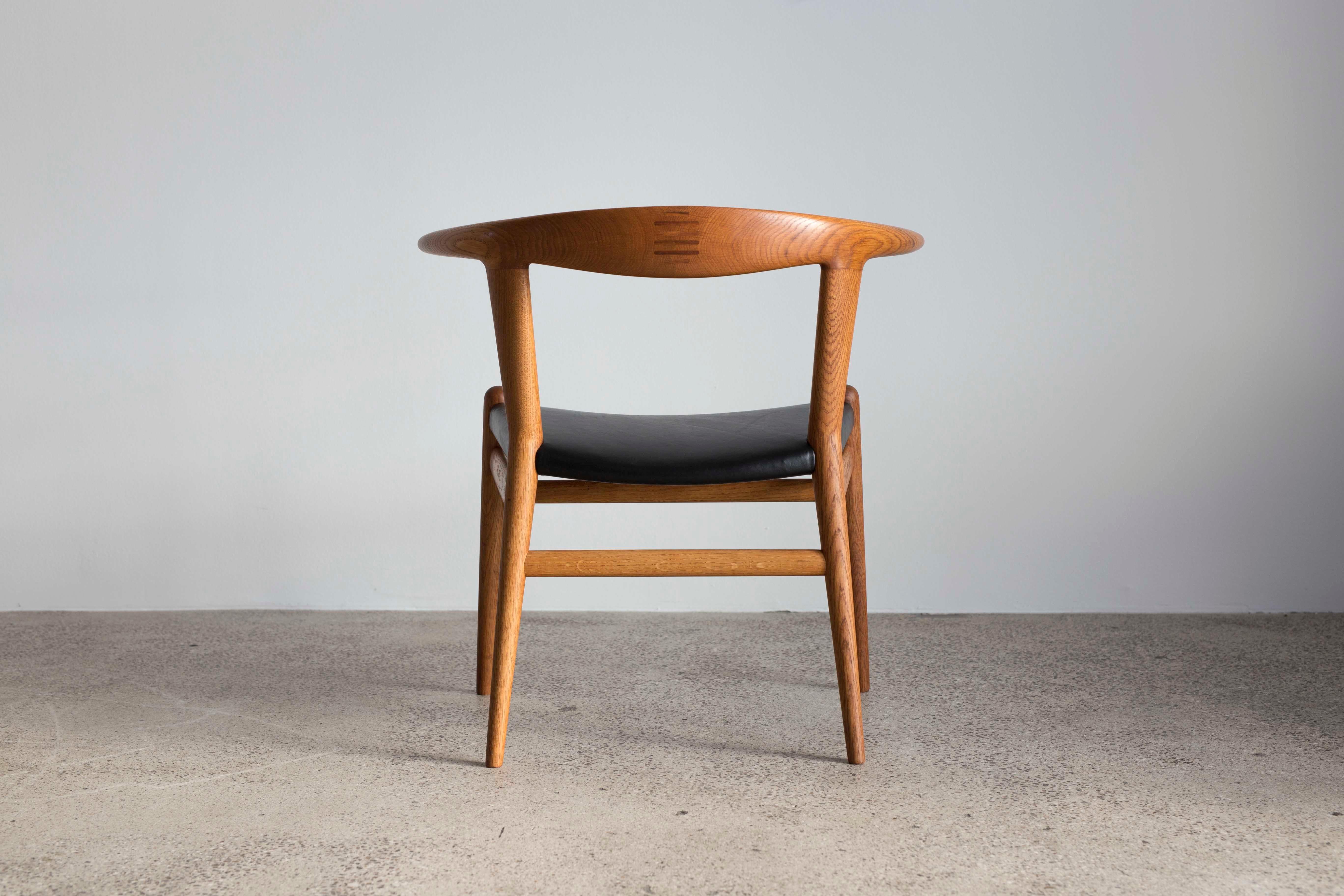 Hans J. Wegner 'Bull Chair' with frame of solid oak and black leather seat.
Designed by Hans J. Wegner 1961, made and marked by cabinetmaker Johannes Hansen, Denmark Model JH 518.