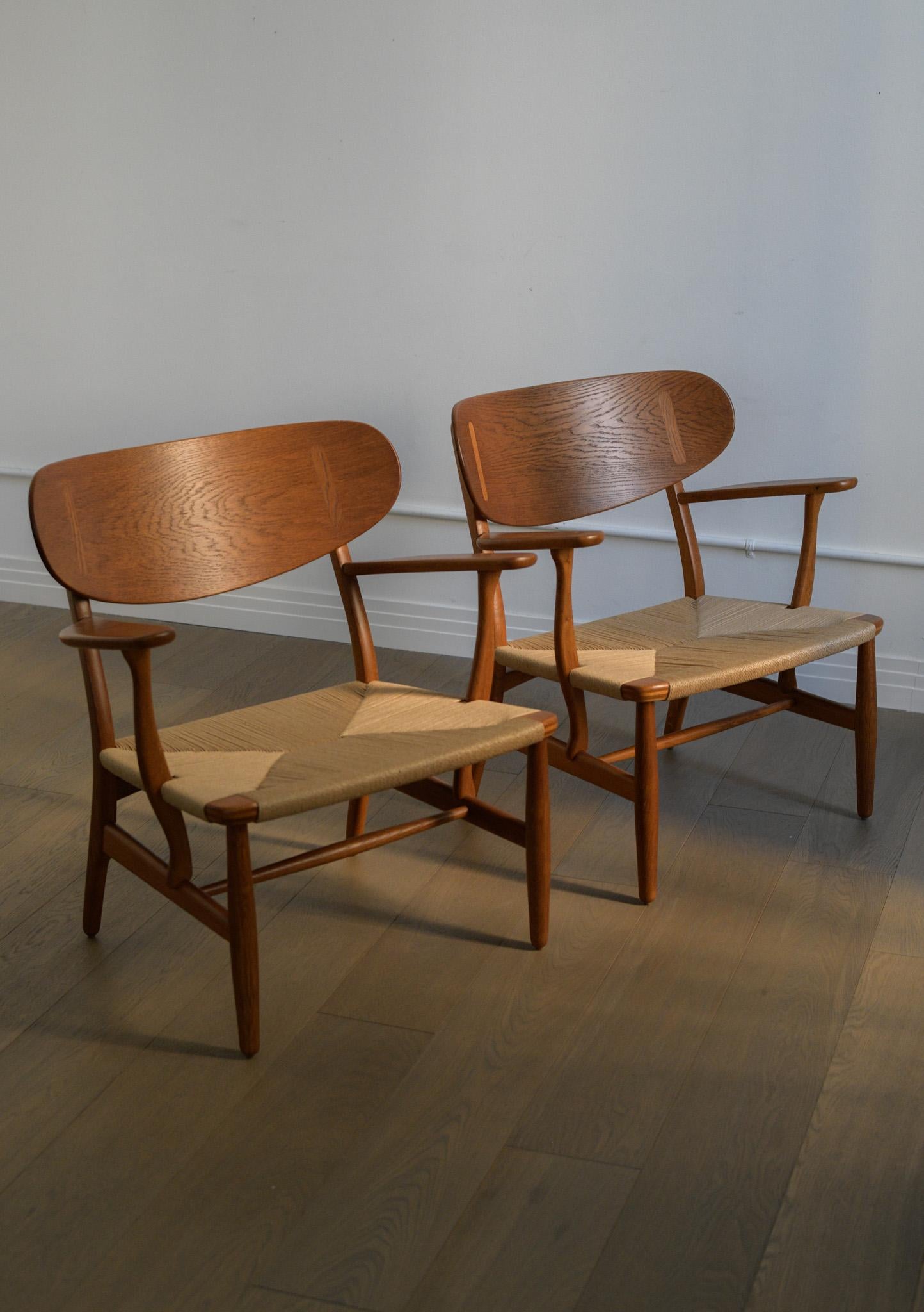 Pair of iconic 1950s Hans J. Wegner CH 22 lounge chairs. 

Professionally refinished and restrung - in great condition and ready to place. 

