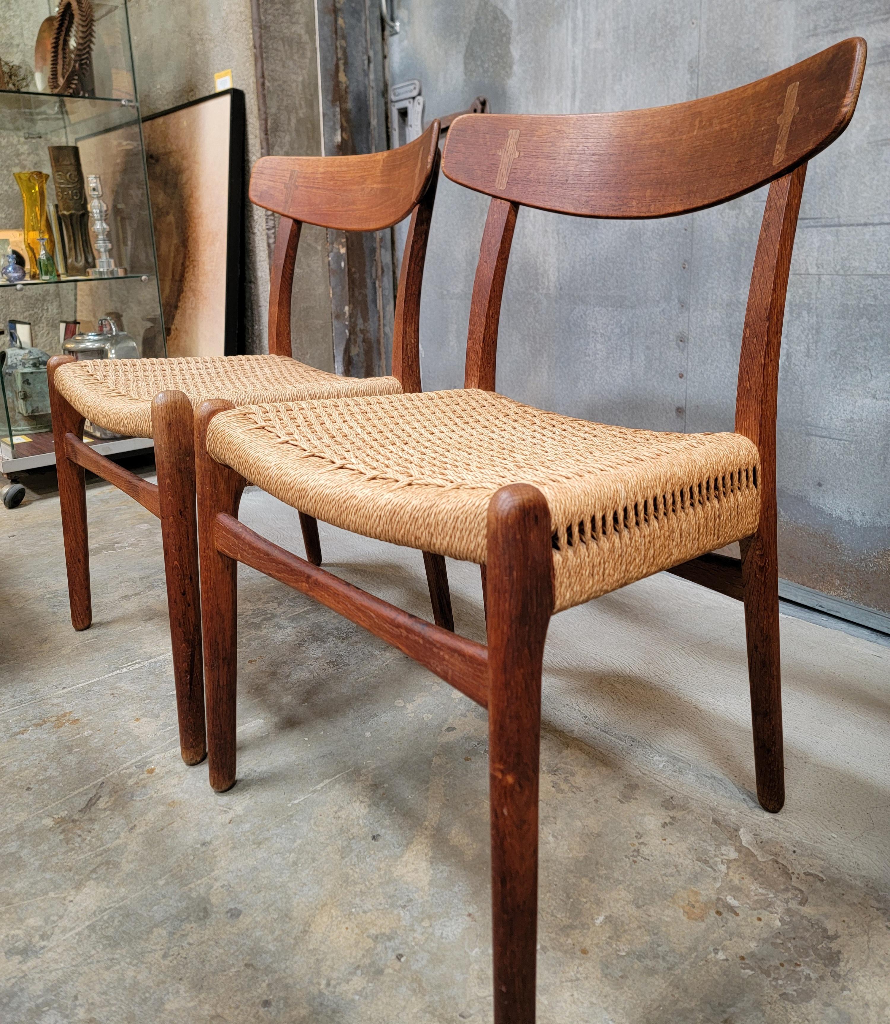 A pair of Danish Modern dining chairs designed by Hans Wegner for Carl Hansen. Denmark, circa. 1950's. Original condition with original seats. Patina and discoloration from age and use to teak frames. Seats in very good condition. Both chairs