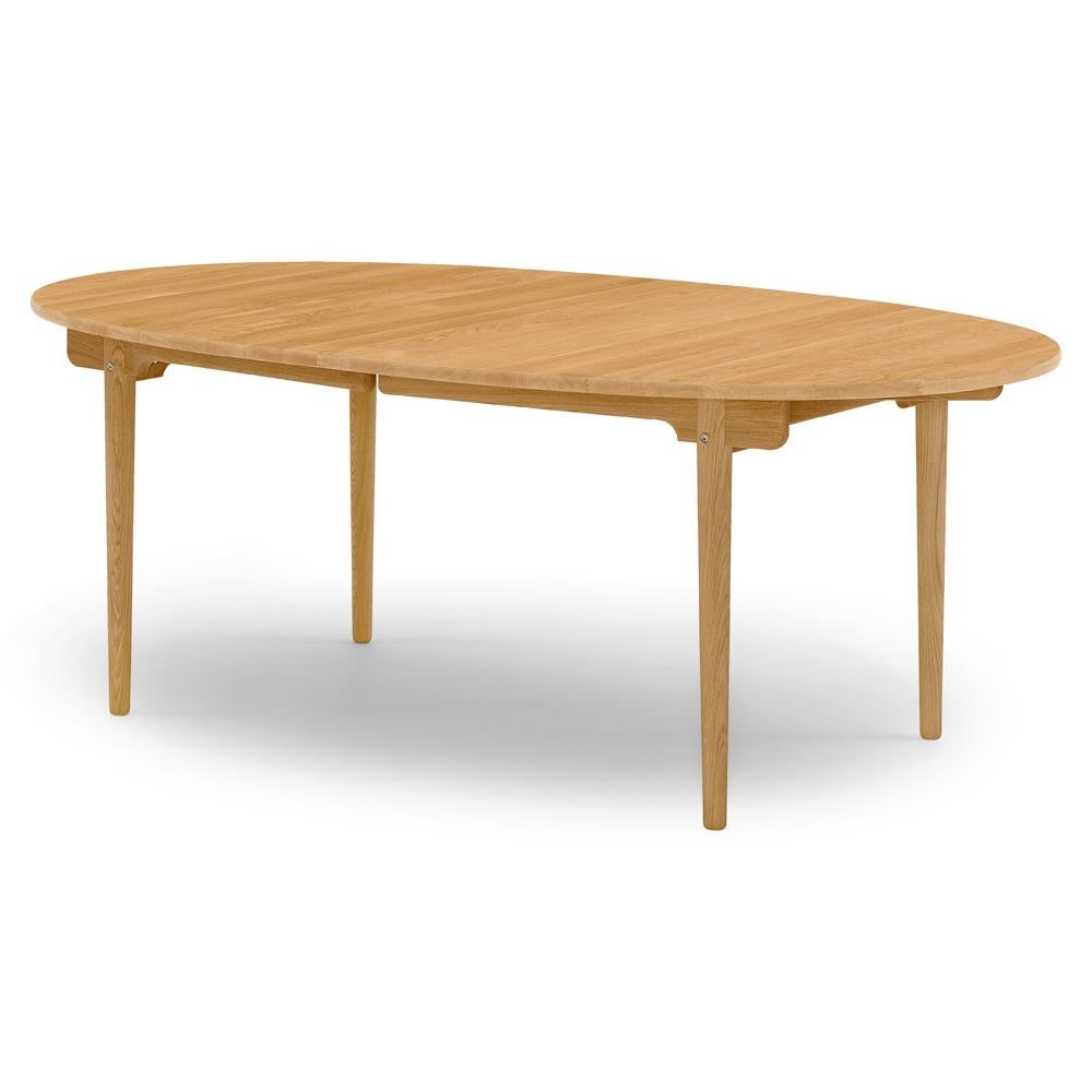 La table de salle à manger CH338, conçue par Hans J. Wegner en 1962, est fabriquée en bois massif et offre la possibilité d'étendre la capacité d'accueil. La table présente un plateau elliptique finement fini et d'élégants pieds fuselés. Son plateau