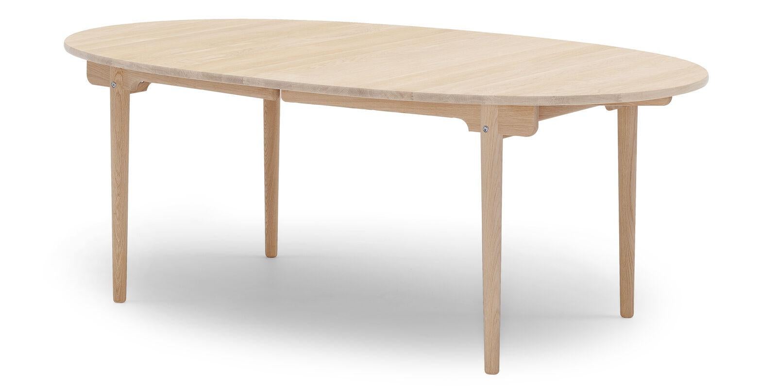 La table de salle à manger CH338, conçue par Hans J. Wegner en 1962, est fabriquée en bois massif et offre la possibilité d'étendre la capacité d'accueil. La table présente un plateau elliptique finement fini et d'élégants pieds fuselés. Son plateau