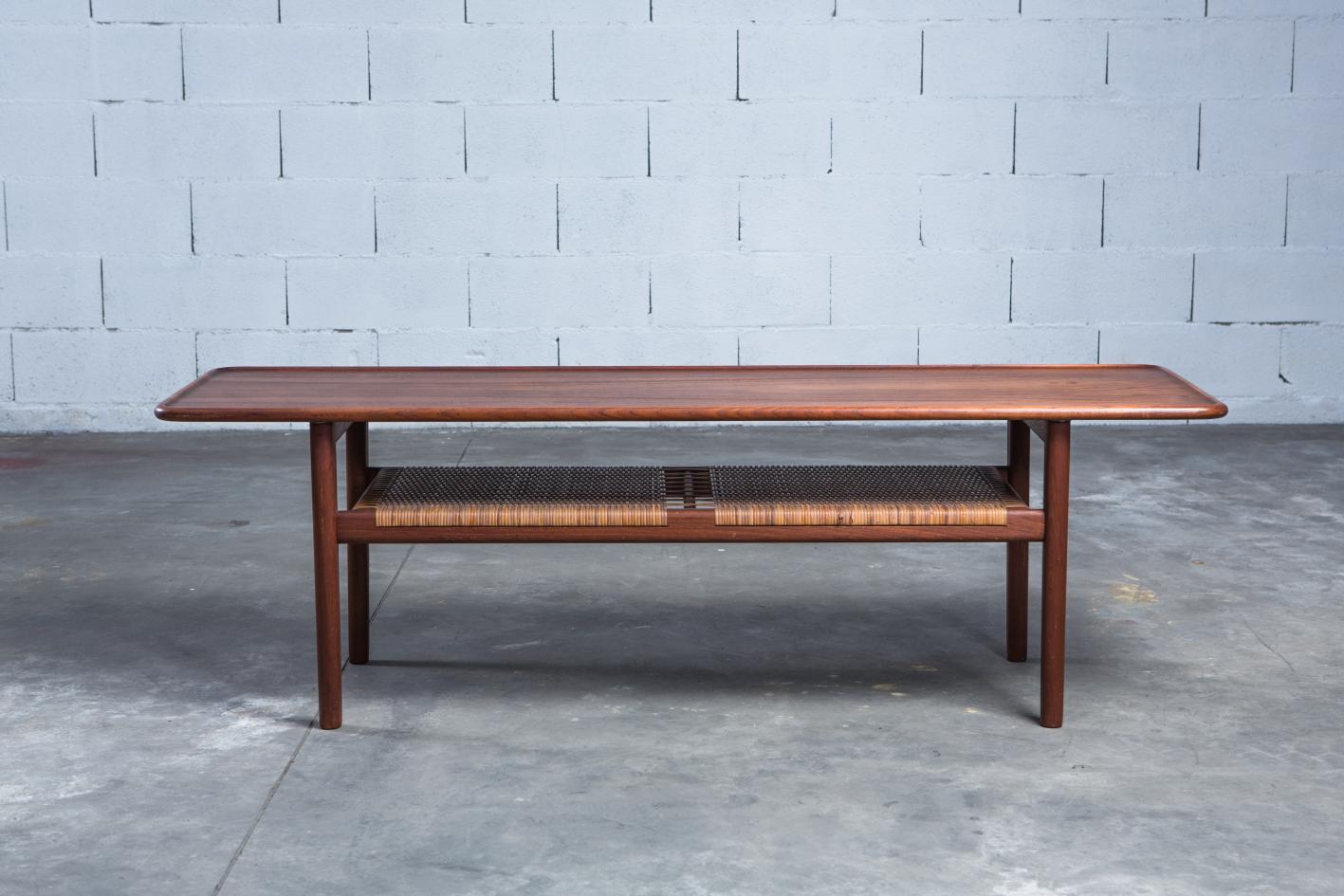 An elegant Danish coffee table model AT-10 in solid teak wood designed by Hans J. Wegner. Made by cabinetmaker Andreas Tuck, Odense - Denmark, in the late 1950s.  The table has beautiful details a teak structure and a shelf/magazine holder in