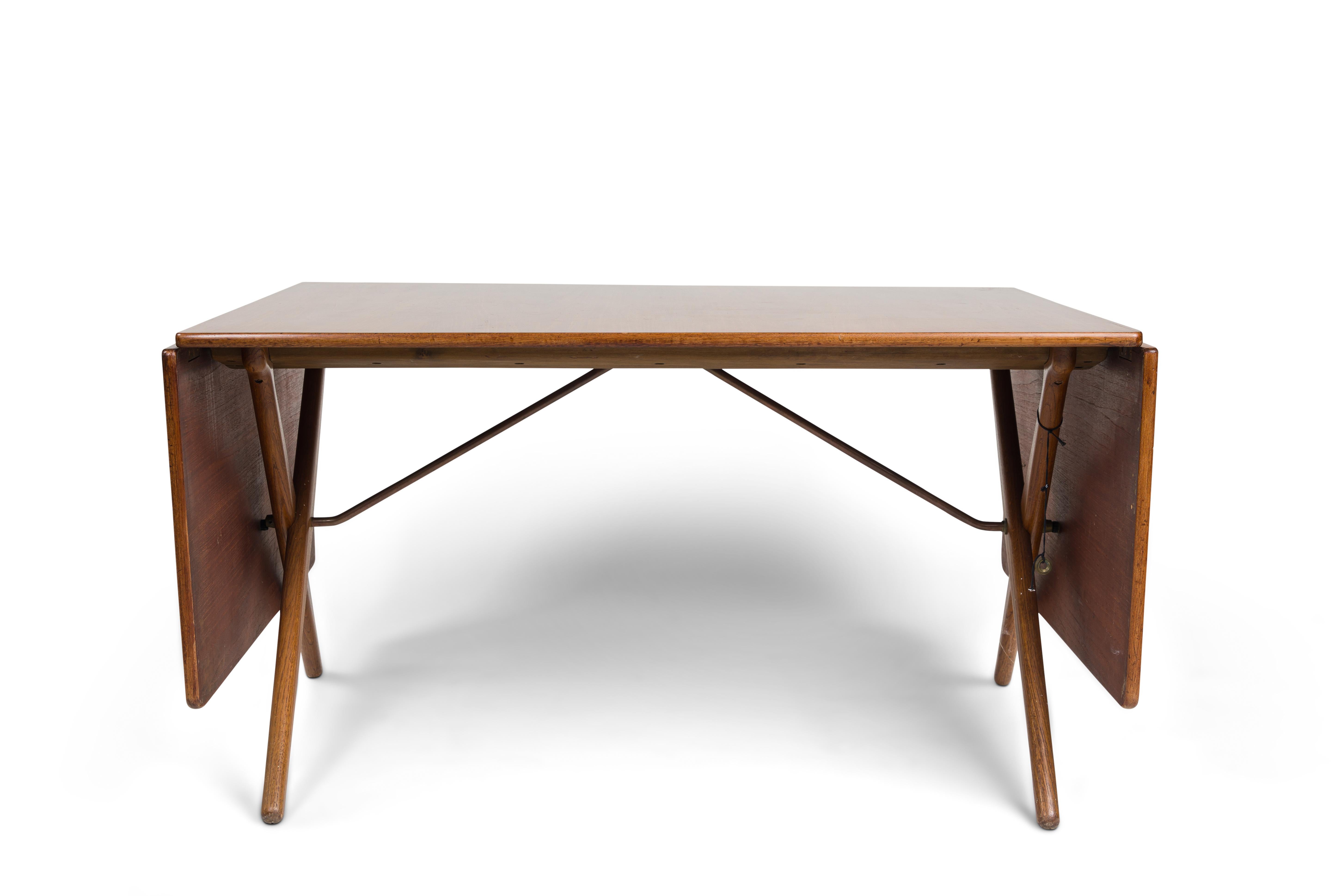 Hans. J. Wegner foldable dining table, model AT304.
Top with varnished teak veneer, with two drop leaves, oak crossed legs and brass struts. Produced by Andreas Tuck with maker's stamp.
Measures: H. 72, L. 128 / 228 W. 86 cm.
Update: the table