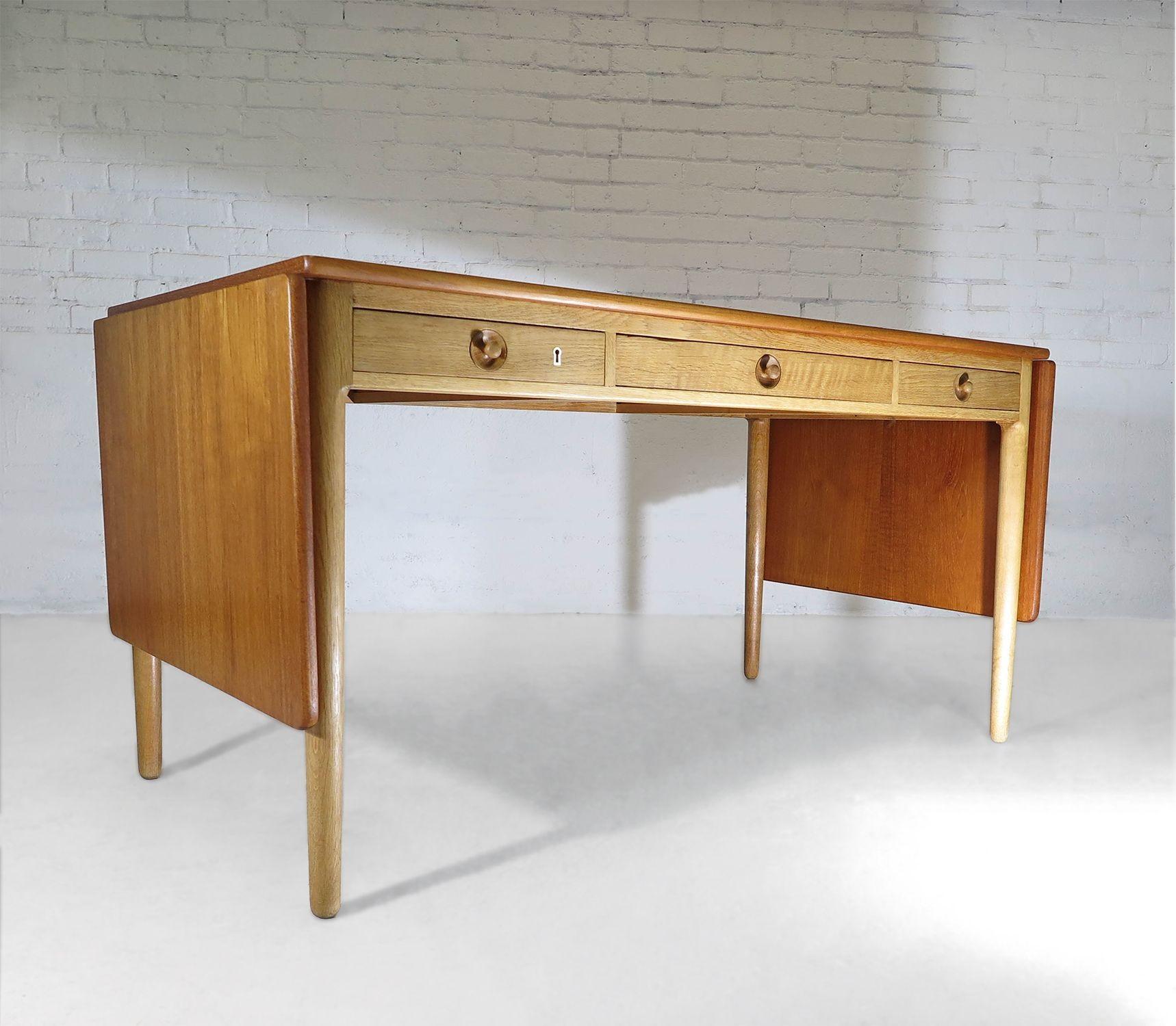Iconic Mid-Century Modern Danish desk designed by Hans J. Wegner for Andreas Tuck, 1955, Denmark. Model AT-305 is handcrafted with a teak top on a solid oak base, featuring three drawers, including a locking left drawer, and drop leaves on either