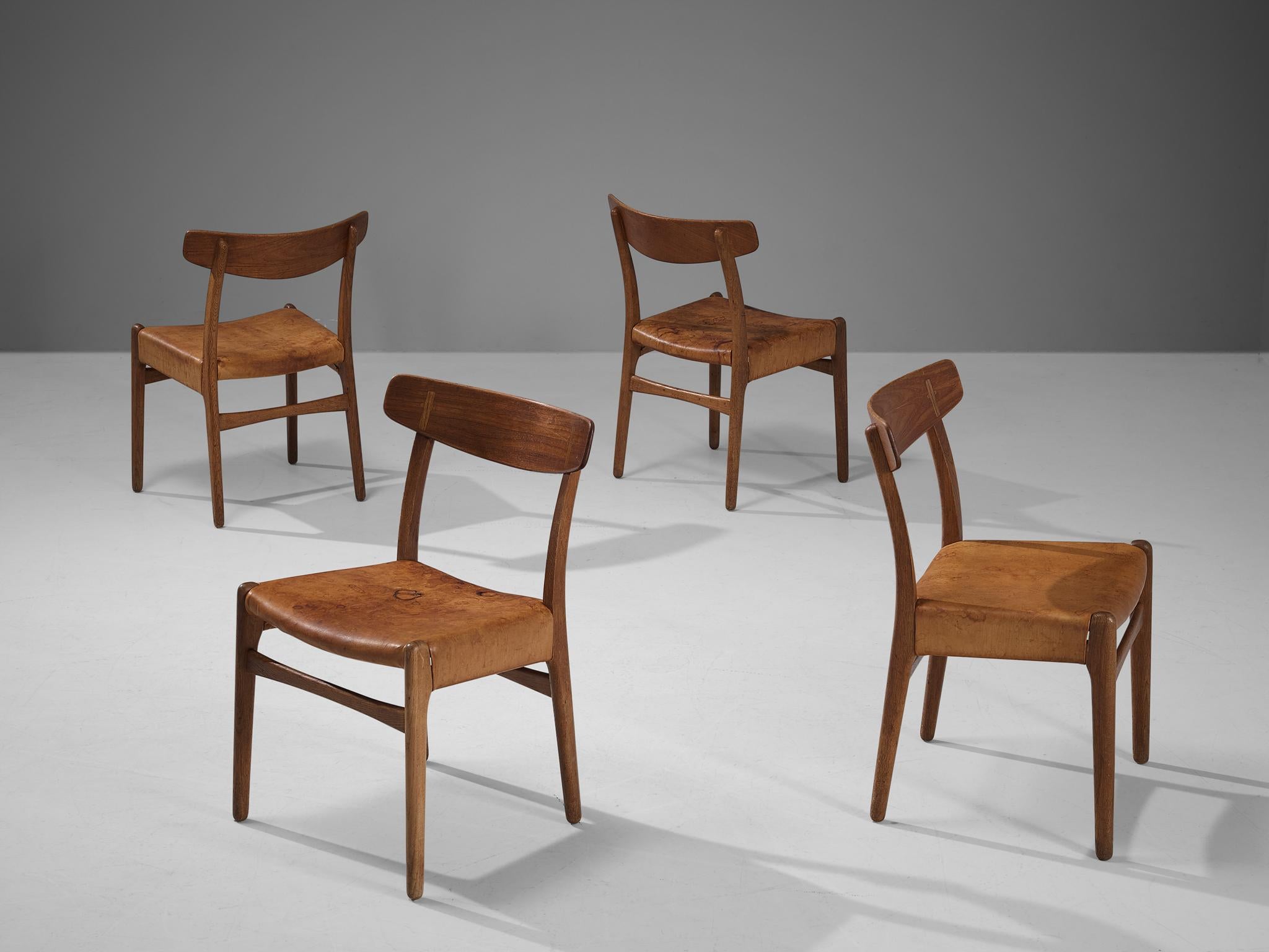 Hans J. Wegner for Carl Hansen, set of four dining chairs, model ‘C23’, oak, teak, cognac leather, Denmark, designed in 1950 

The chair model ‘C23’ features sophisticated details that characterize Wegner’s well-known designs. Per example, note the