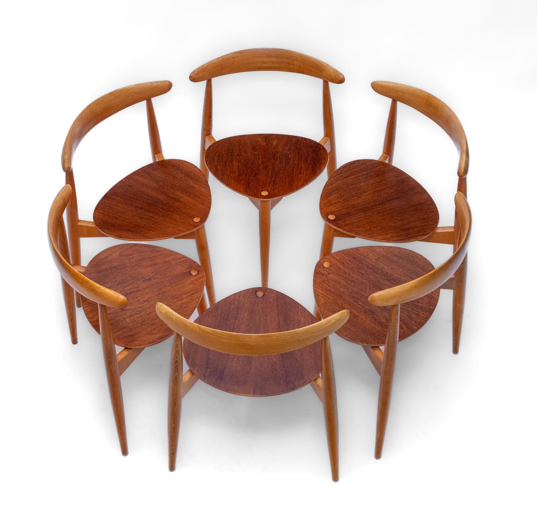 Danish mid century set of six teak and beech stackable heart tripod dining chairs and matching tripod circular dining table. Design by Hans Wegner for Fritz Hansen. Circa 1955. Maker's marks.

A renowned space-efficient mid century design, the
