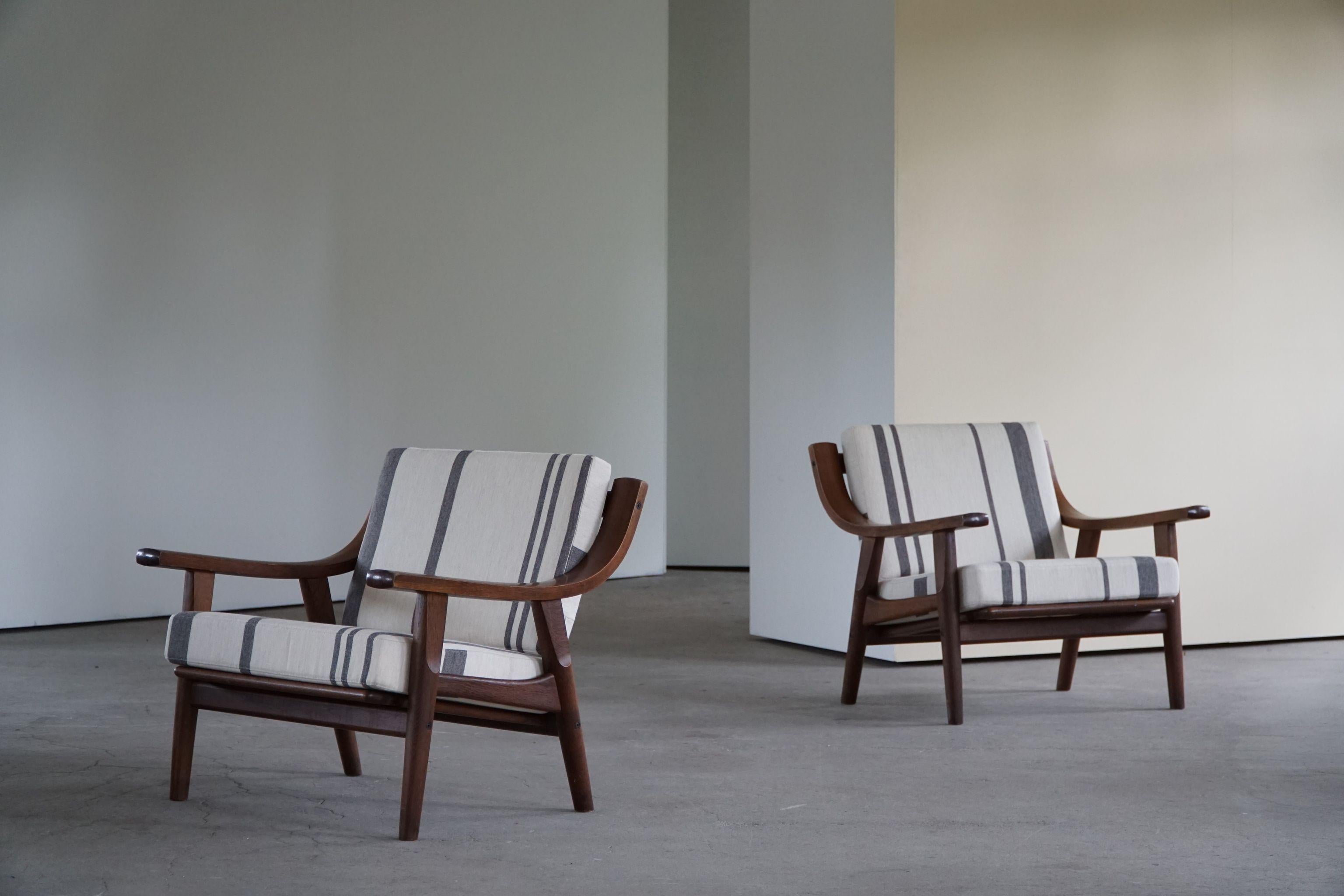 A fine pair of lounge chairs in solid dark stained oak, reupholstered cushions in great quality striped savak wool. Designed by Hans J. Wegner for Getama, model 