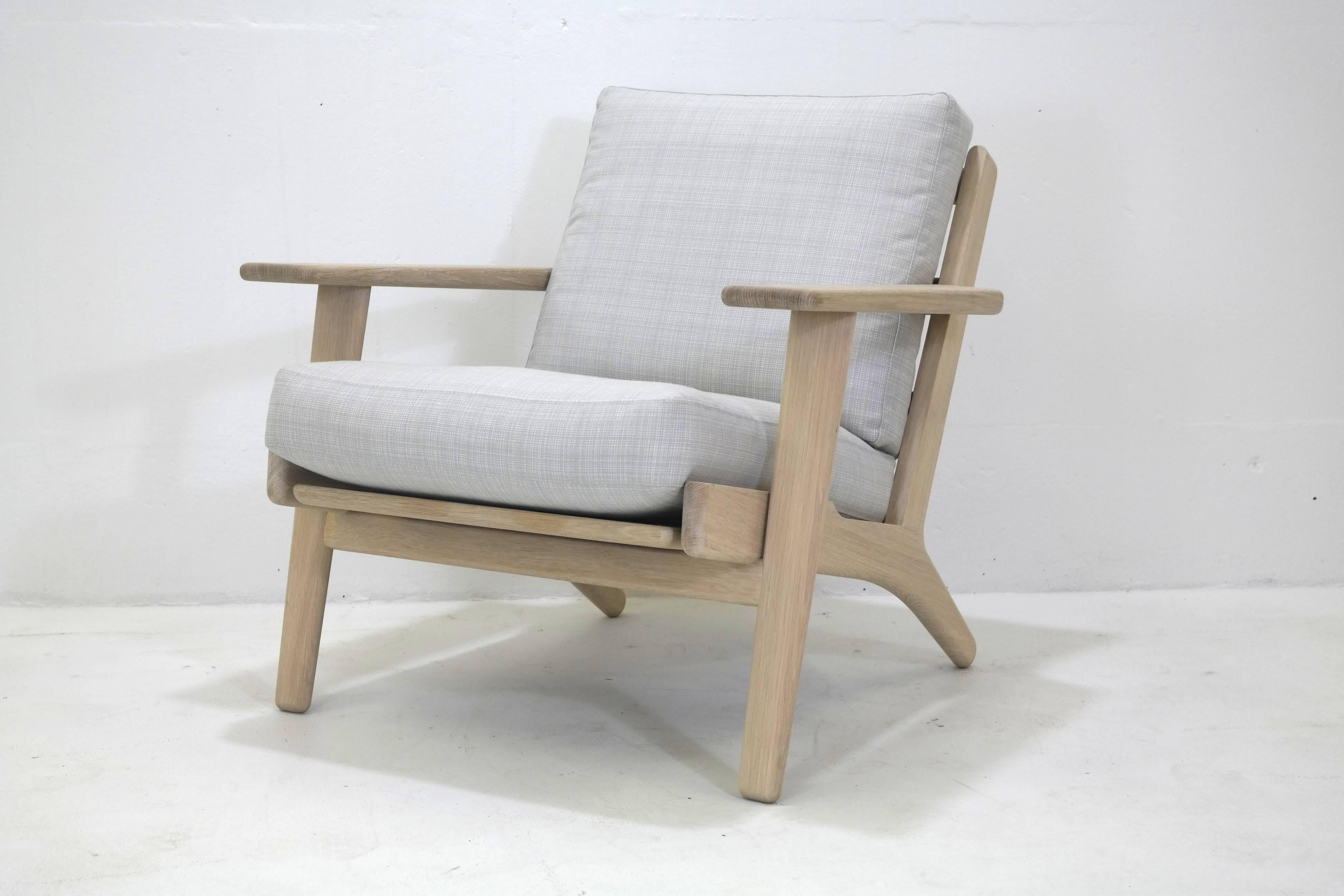 This chair is designed by Wegner in 1953 and re-issued today by the original manufacturer GETAMA of Denmark. The easy chair is featured in natural oak with off-white linen/down filled cushions. We welcome custom orders. Each piece is handmade in