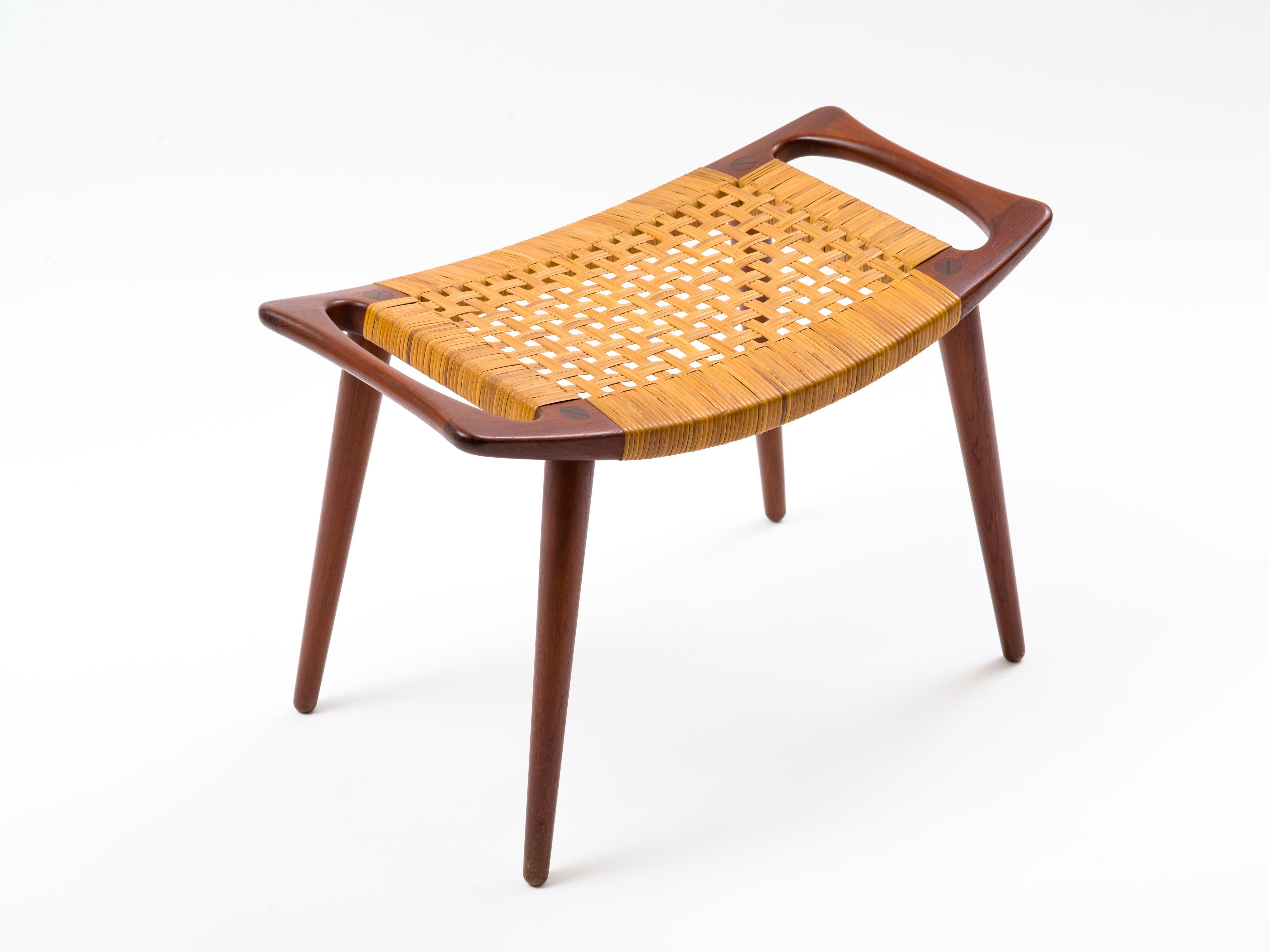 A handled stool, model JH 539, in solid teak with caned seat by Hans Wegner and built by cabinetmaker Johannes Hansen. In lovely, all original condition, this example retains its original caning which exhibits just a few small, inconspicuous breaks.