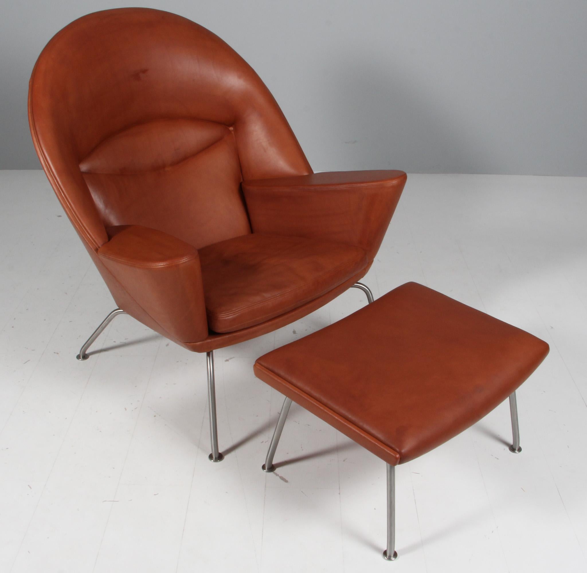 Hans J. Wegner lounge chair and ottoman in brandy full grain aniline leather.

Legs of brushed stainless steel.

Model Oculus, made by Carl Hansen.