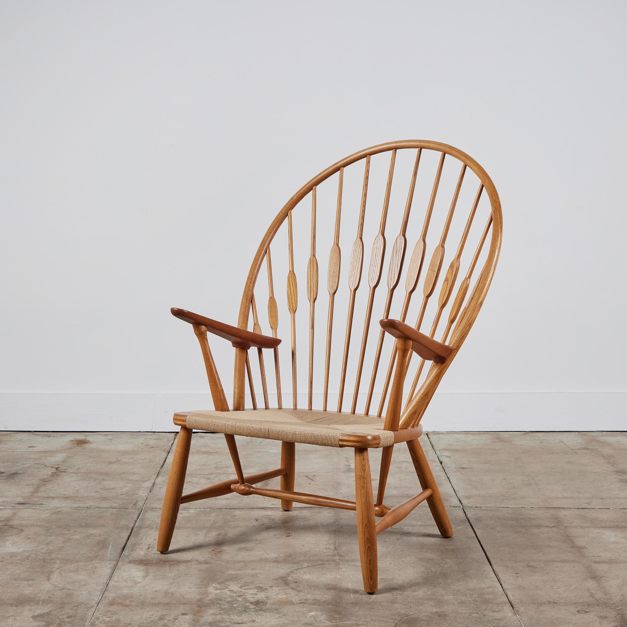 Designed in 1947, this fully restored Hans Wegner peacock chair features Windsor chair styling and characteristic attention to detail. The solid oak and teak frame has a high, arched back strung with round wooden supports that flatten where the