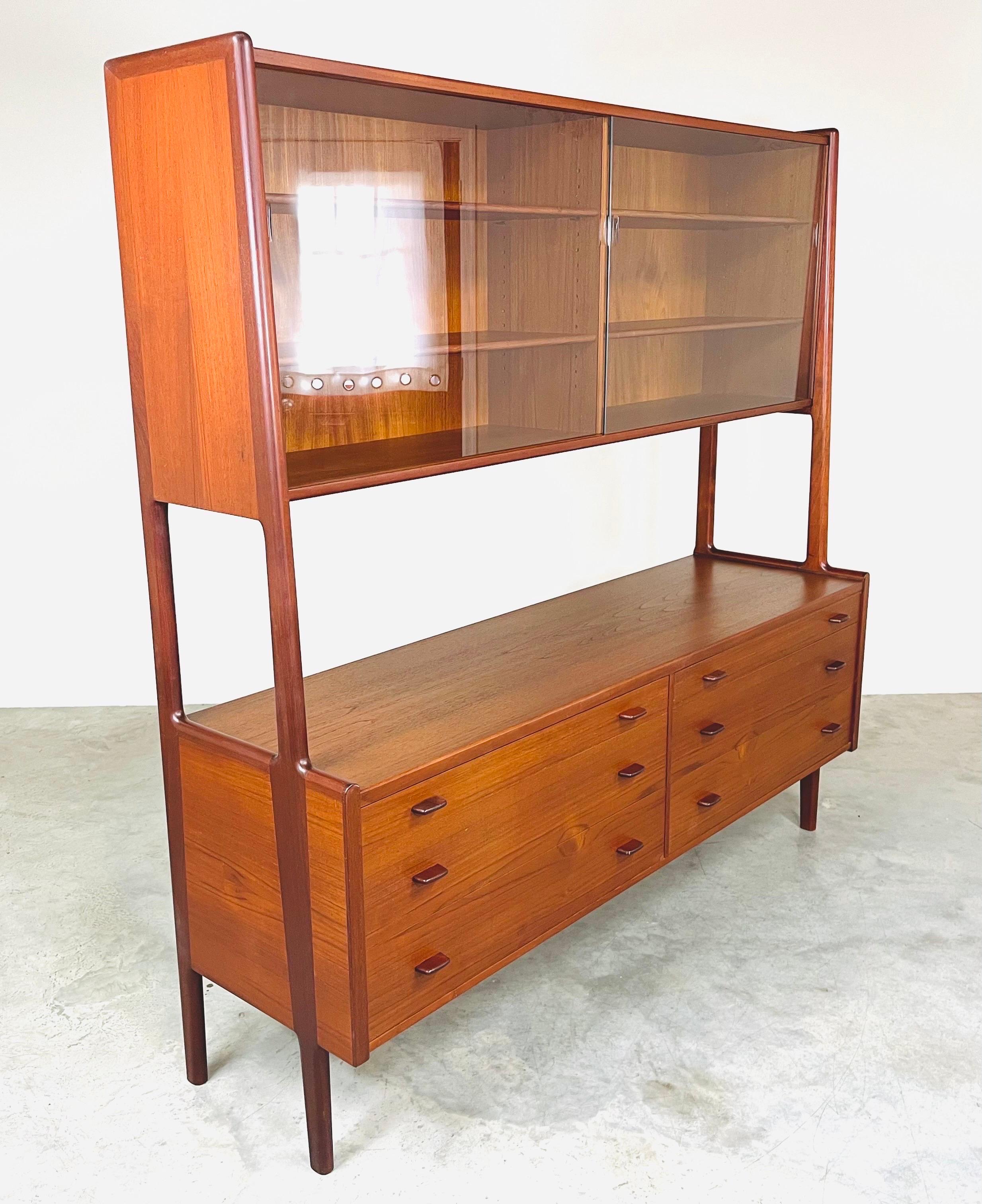 A sculptural teak Danish Modern credenza having top hutch that is connected by solid teak legs that run from floor to top designed by Hans Wegner circa 1957. This cabinet features 6 drawers with book matched fronts and 4 shelves that rest behind