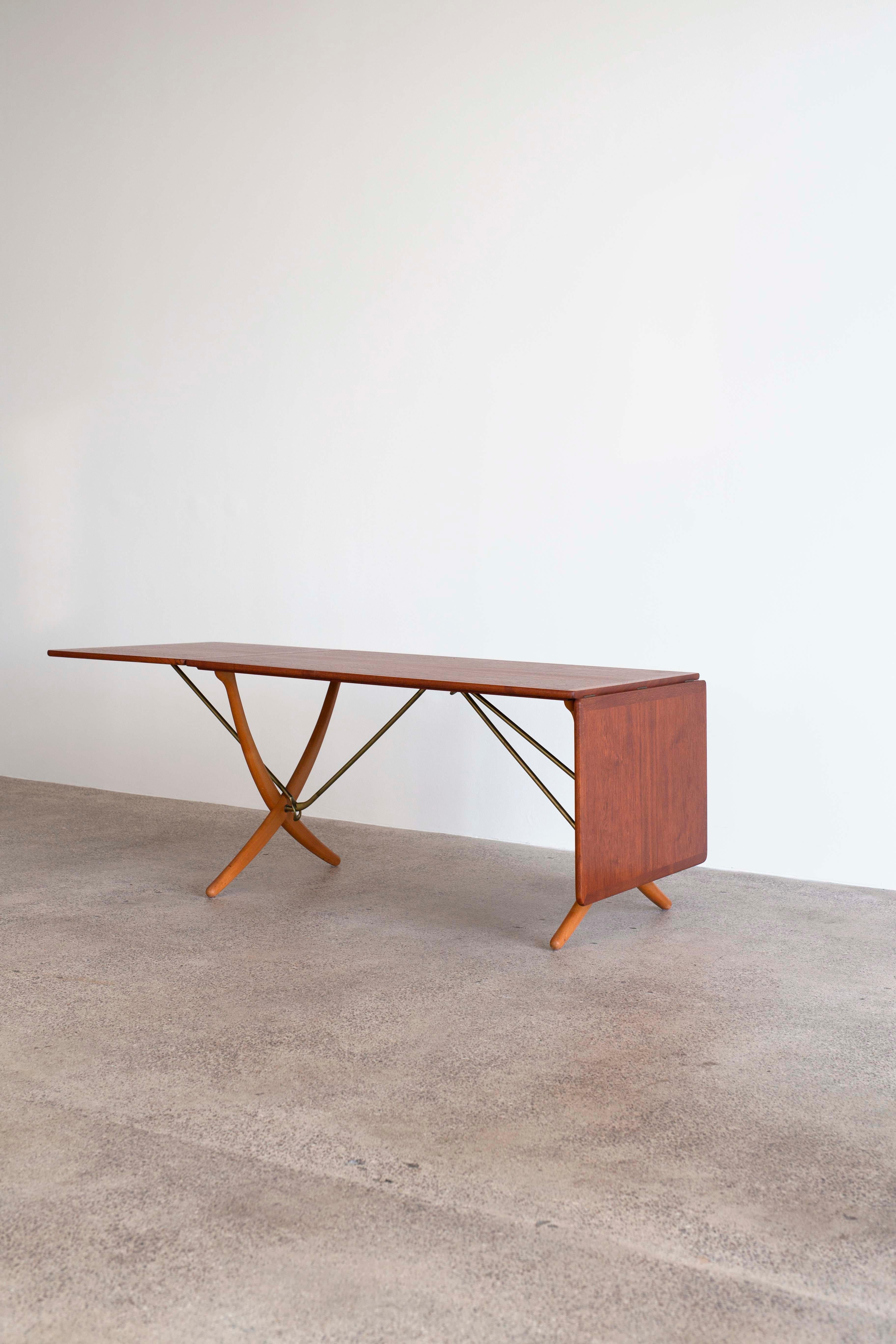Hans J. Wegner teak dining table with two drop-leaves, cross-legs of patinated beech and stretchers of brass. Very fine condition. 

Designed by Wegner 1950 and manufactured by cabinetmaker Andreas Tuck, Denmark, model AT304. 

Measuring 128 cm