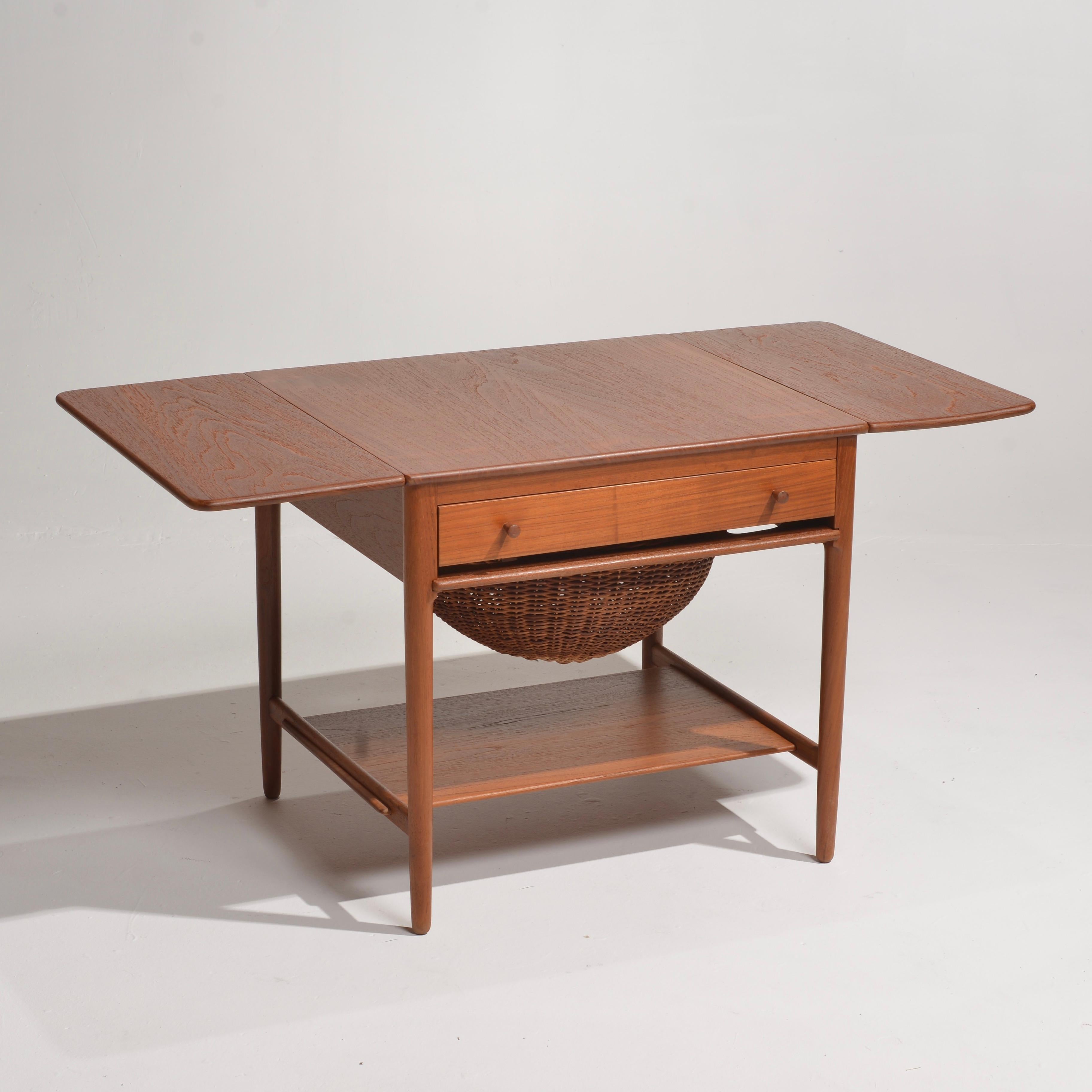 Magnifique table de couture modèle AT-33 conçue par Hans Wegner et fabriquée au Danemark par l'ébéniste Andreas Tuck. Cette table en teck et en chêne est dotée de deux allonges, d'un tiroir avec compartiments pour les articles de couture, d'un