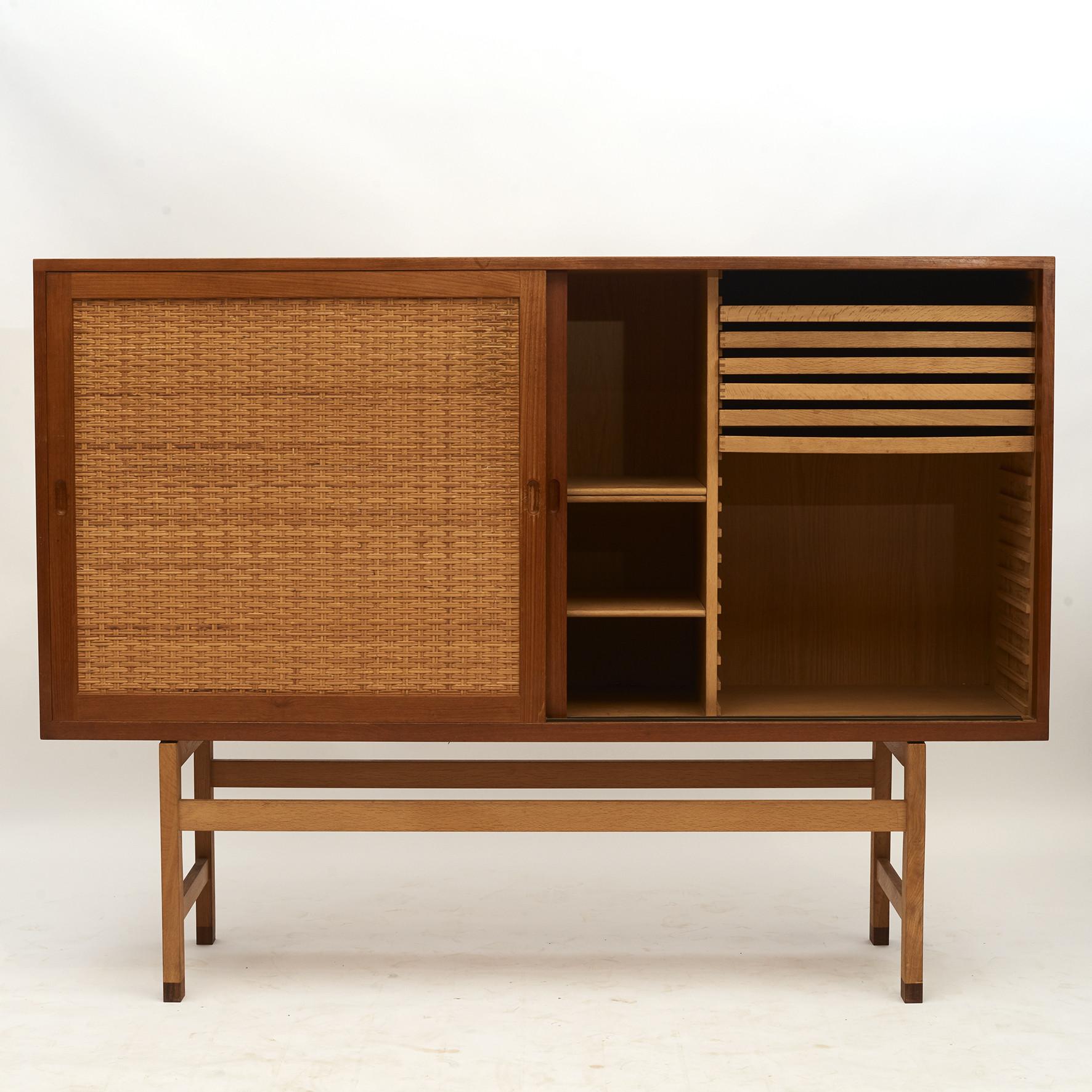 Hans J. Wegner.
Tall sideboard or cabinet in oak veneered in teak with sliding doors in cane. Solid oak base with rosewood feet.
Behind the doors you will find storage space with shelves and sliding trays.
Manufacturer: Ry Møbler, Denmark,