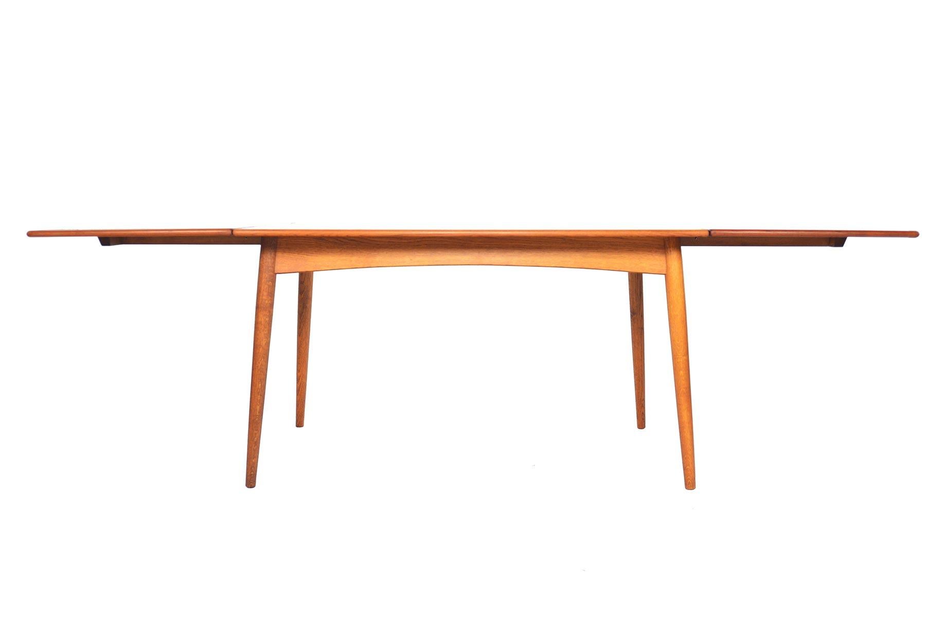 This stunning Danish modern dining table was designed by Hans J. Wegner for Andreas Tuck in the 1950s. The beautifully banded teak table top stands on a solid, quarter- sawn oak base. Each side of the table offers hardware to support leaves. Table