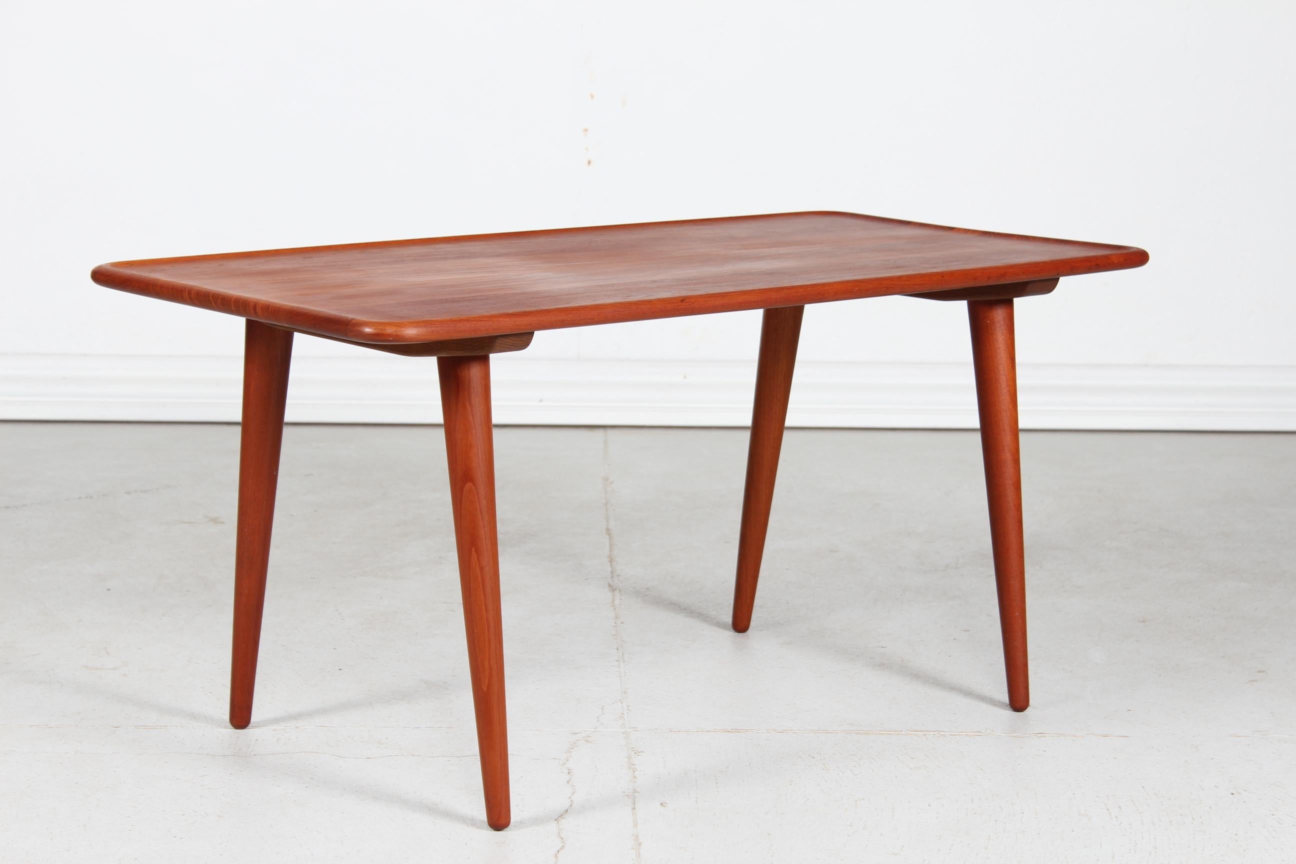 Table basse vintage modèle AT 11 de l'architecte danois Hans J. Wegner (1914-2007) fabriquée par Andreas Tuck dans les années 1950.

Table basse oblongue en teck massif traité à l'huile. Le plateau de la table a un bord surélevé et les pieds