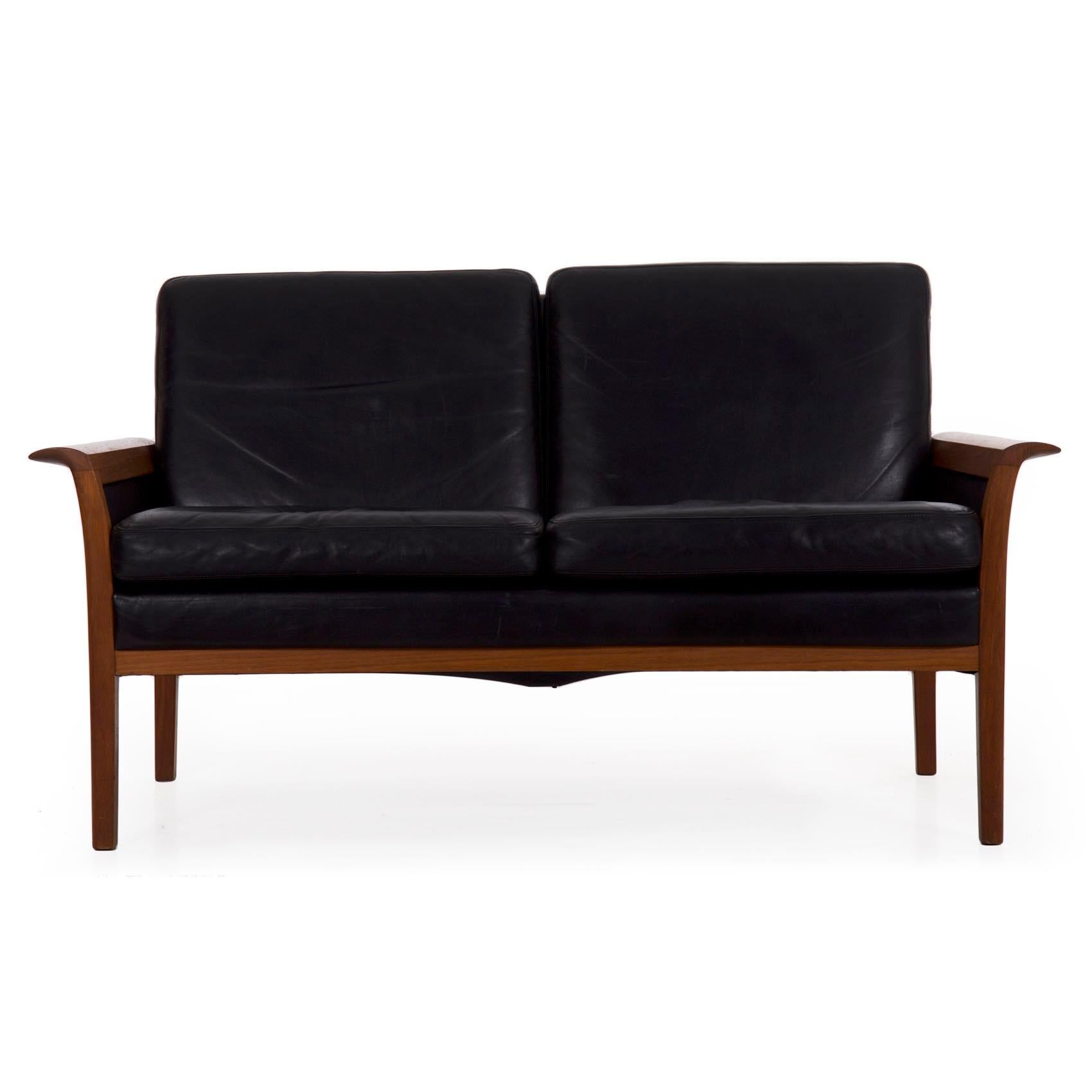 A very attractive two-seater loveseat sofa designed by Hans Olsen and retailed by Vatne Møbler during the third quarter of the 20th century, it retains its original thick black leather upholstery throughout. The sculpted teak frame is particularly