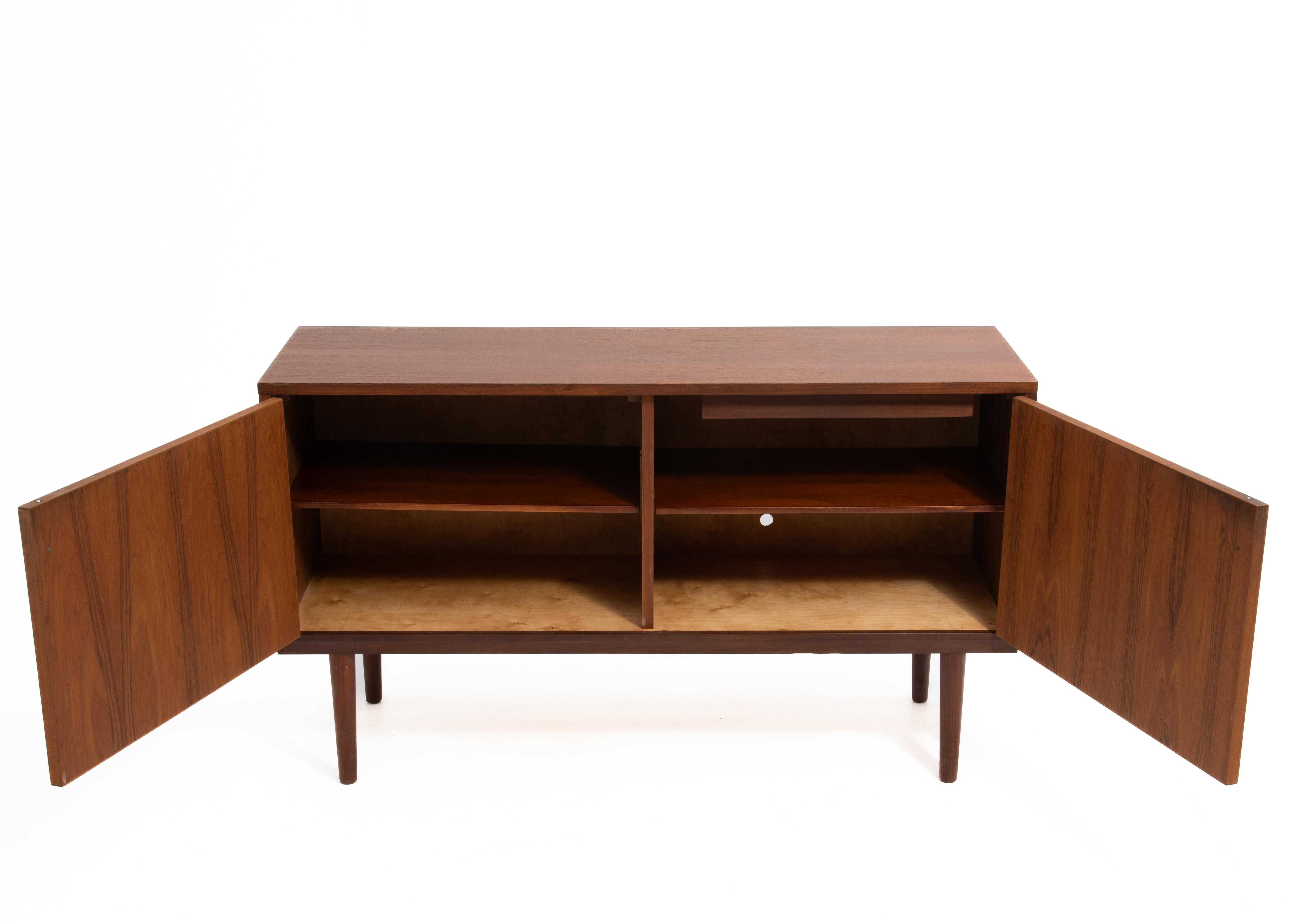 A petite teak credenza designed by Hans Olsen and made in Denmark. A great size that works in a living room as an entertainment console  or dining room as a buffet/credenza. The two doors open from the center to reveal adjustable shelves. Fully