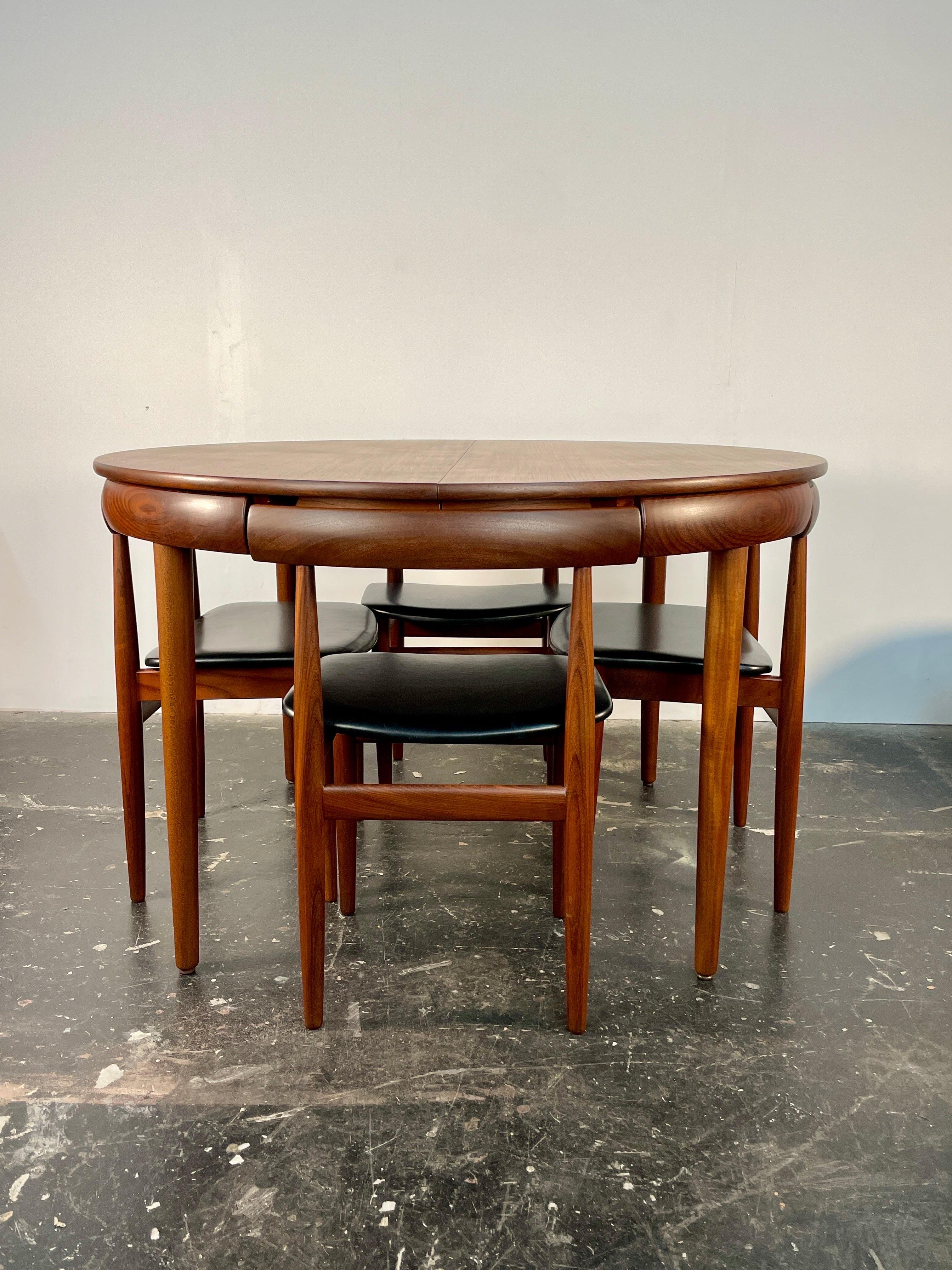 This exceptional Mid-Century Danish Modern dining set, designed by Hans Olsen for Frem Røjle in the 1950s, showcases innovative craftsmanship and space-saving functionality. The teak and Afromosia (African teak) dining table features a clever