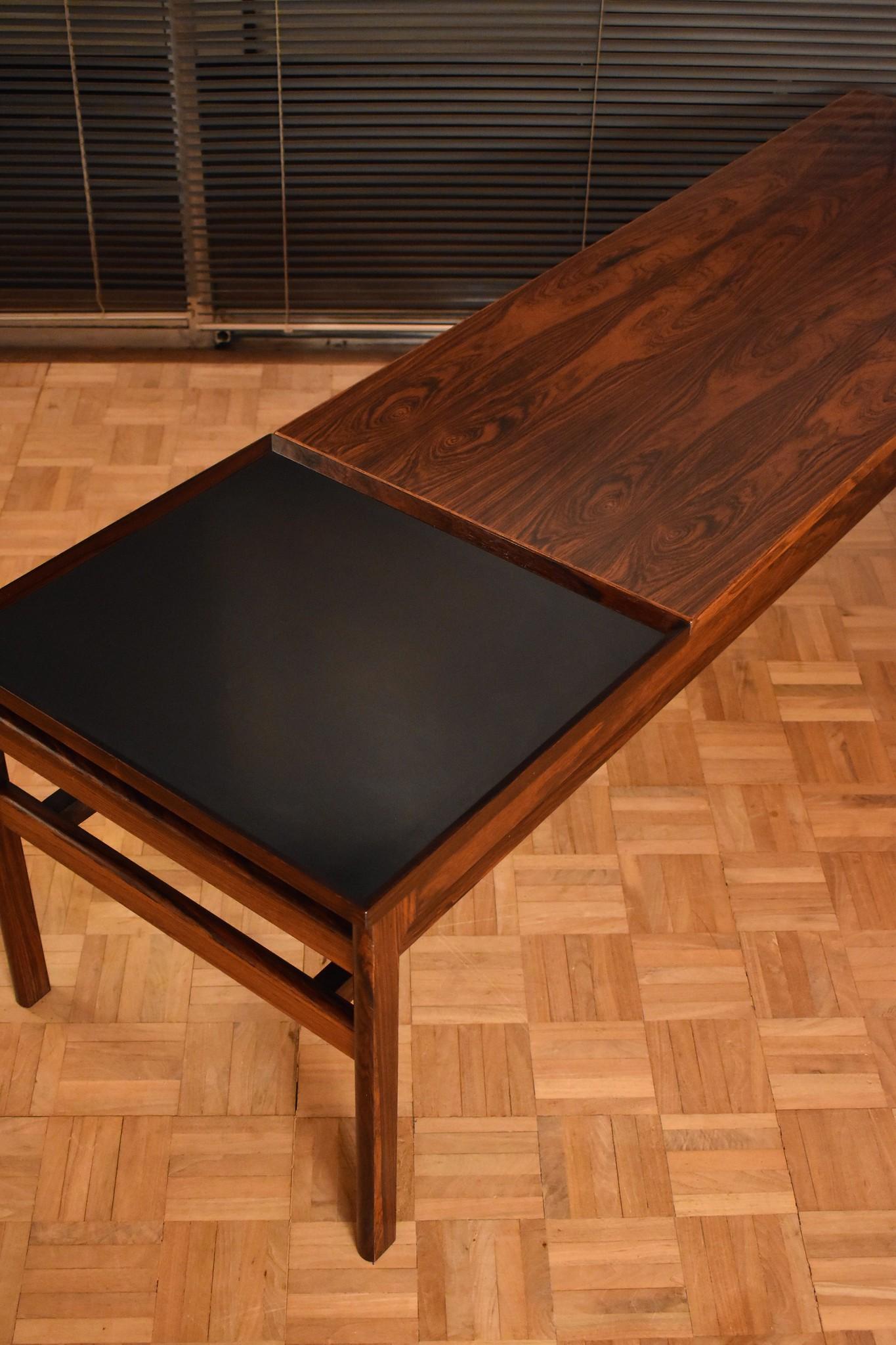 An incredibly rare design from Hans Olsen.

A very impressive coffee table produced in lush Brazilian rosewood. The design features a sliding surface which allows a black melamine tray stowed underneath to be placed on top. This hard wearing