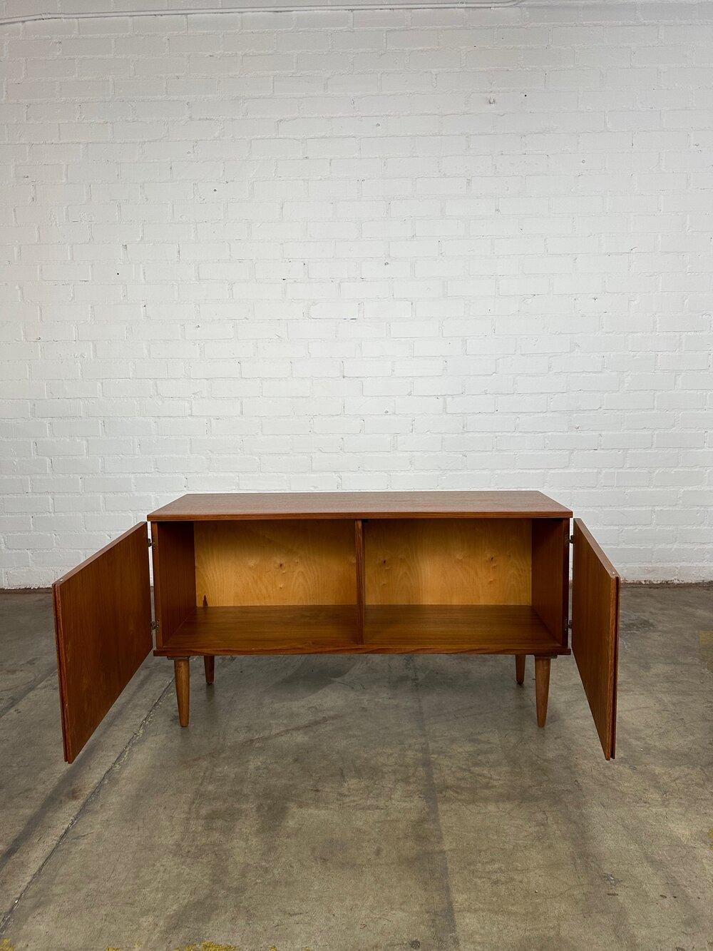 Measures: W50 D17 H27.5

Restored teak credenza with ambrosia teak details in a low profile design. The doors open out via the sculpted recessed detail in the center. The interior is open storage with no included shelves. We can include shelves at