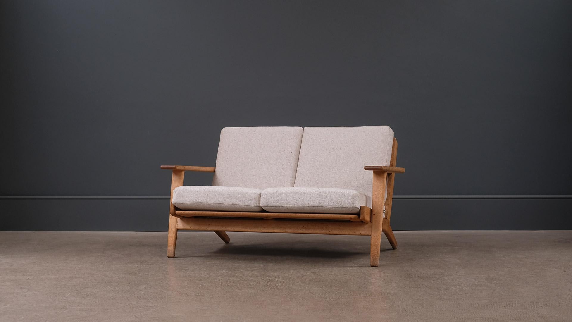 Classic two-seat sofa model GE290 designed by Hans Wegner for GETAMA, Denmark. Solid oak frame with fully reconditioned and reupholstered original sprung cushions.