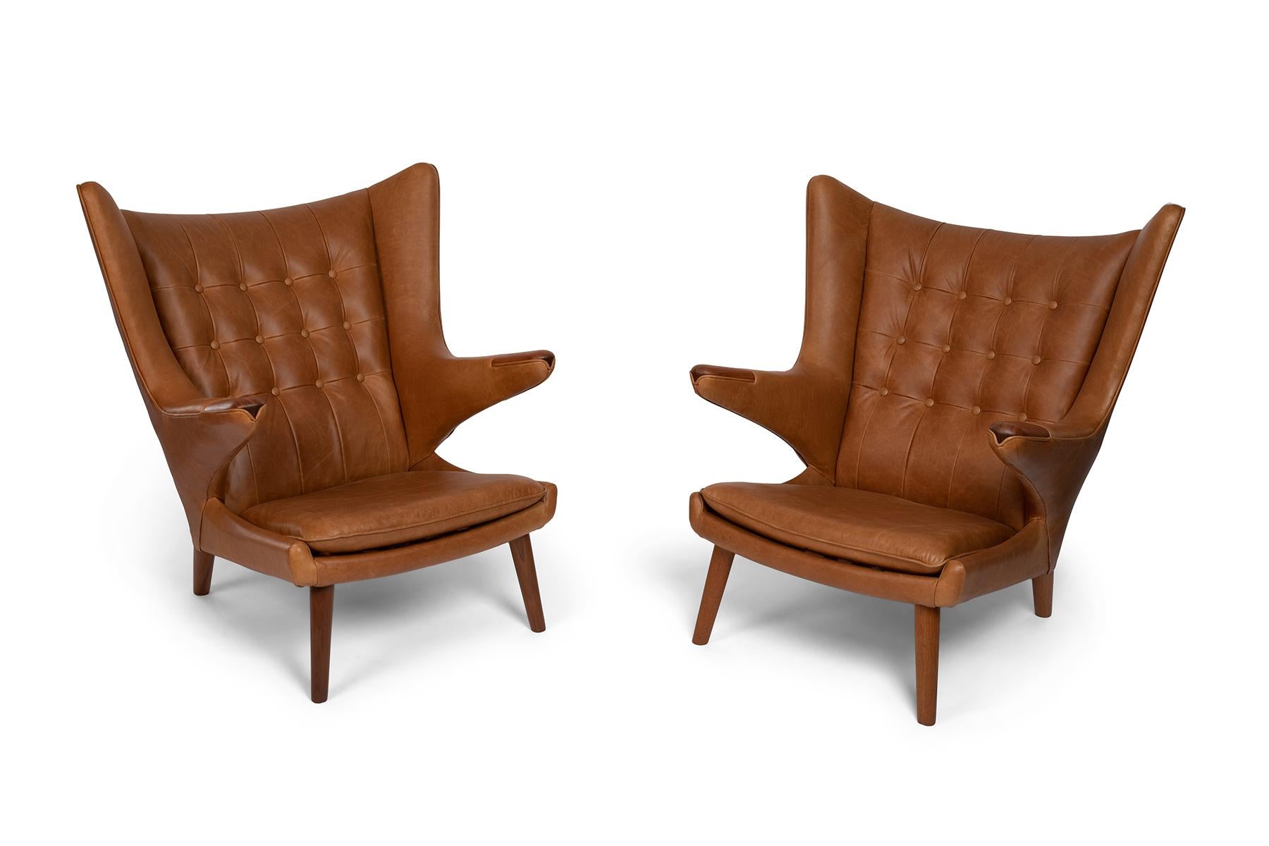 Pair of Hans Wegner A.P. stolen papa bear chairs and ottoman from 1951. These sculptural examples have solid teak paws, legs and ottoman sides. This set has been newly and masterfully upholstered in a stunning caramel leather. Price listed is for