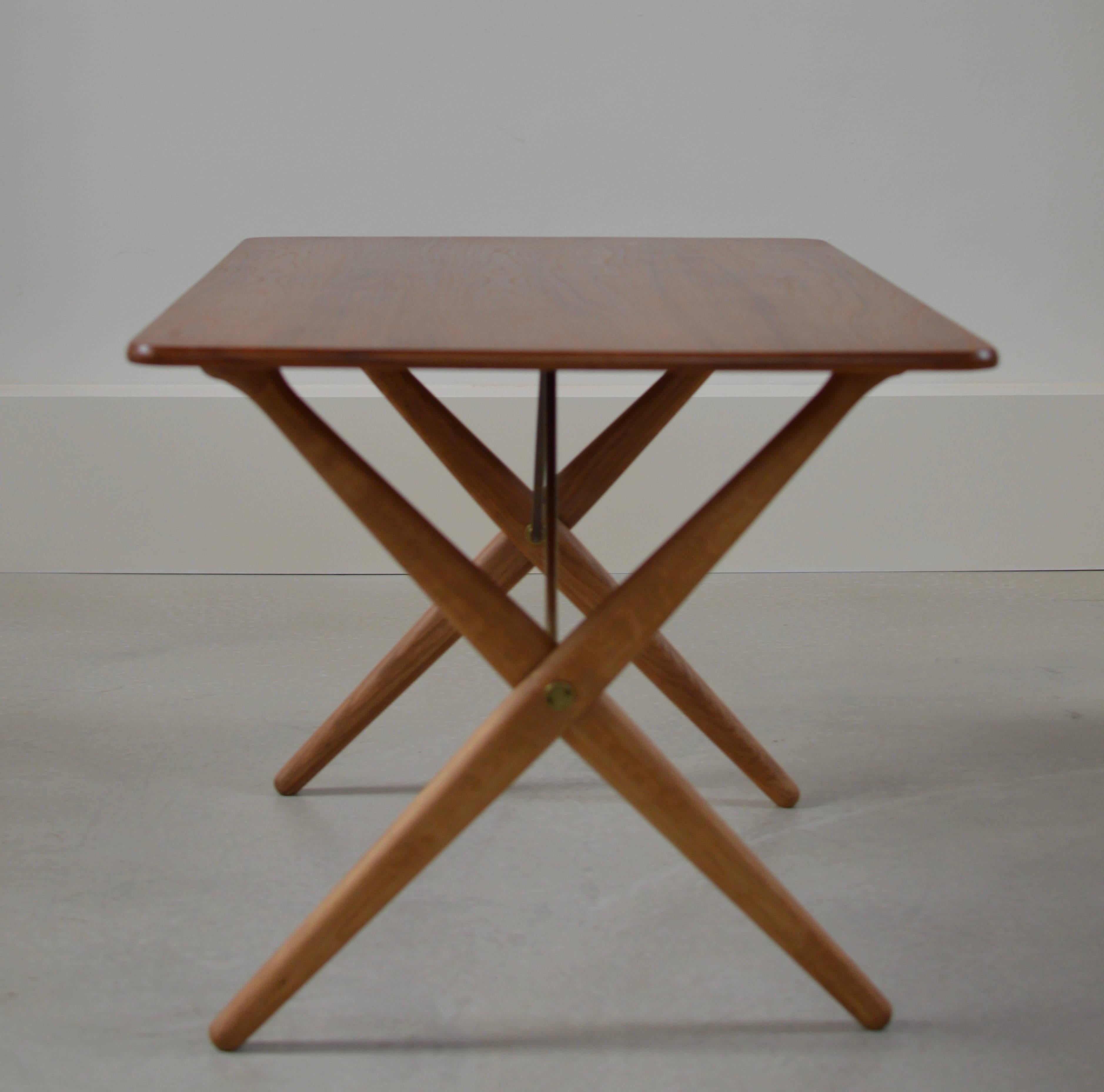 Smaller cross legged table by Hans Wegner for Andreas Tuck, model AT 308 designed in 1955 for Andreas Tuck, as signed with burn mark. 
Table top of teakwood with contrasting cross legged base of solid oak with brass stretchers.

A versatile piece