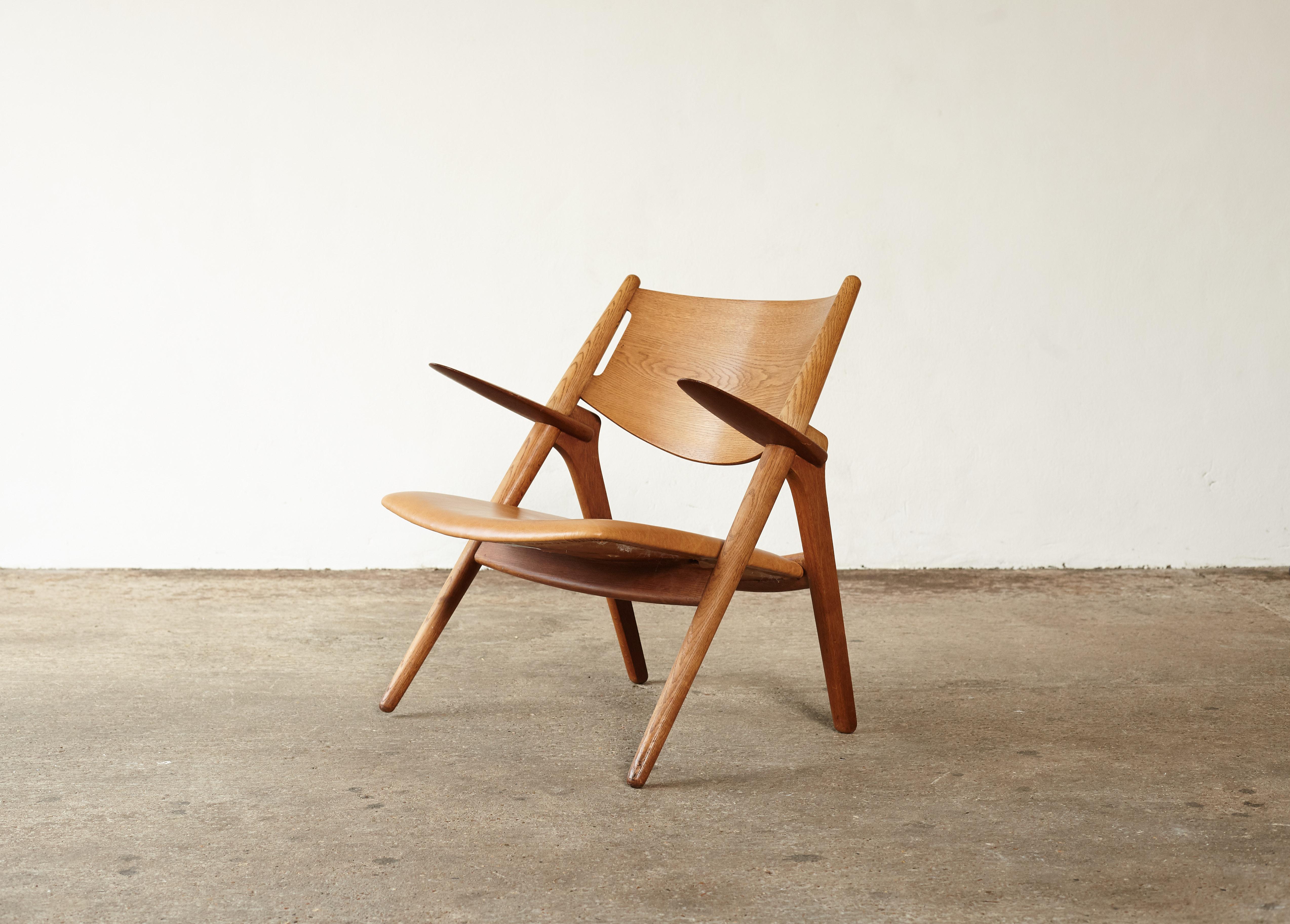 A super example of the Classic Hans Wegner CH-28 sawbuck armchair. Oak frame, with lovely grain, and tan leather seat. Ships worldwide.